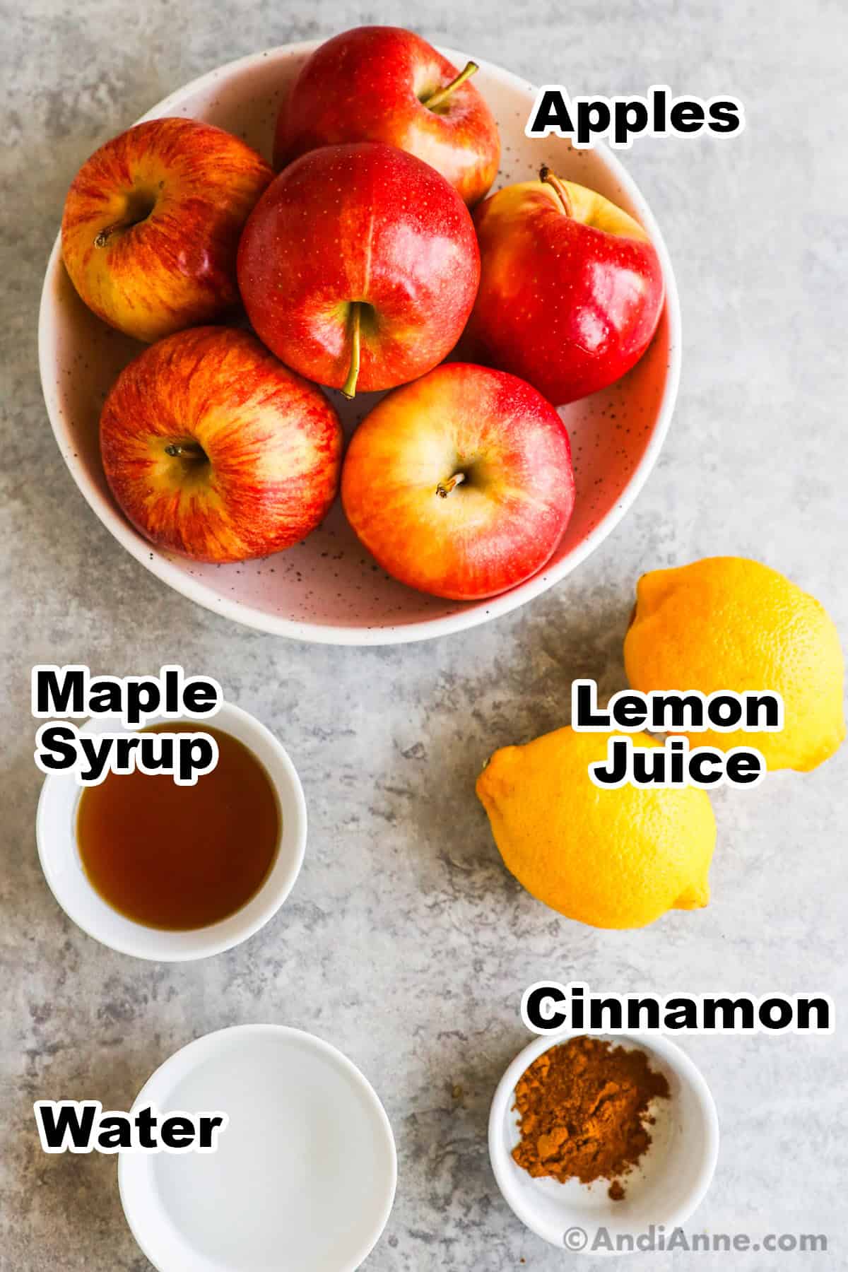 A bowl of apples, some lemons, and small bowls of maple syrup, cinnamon and water.