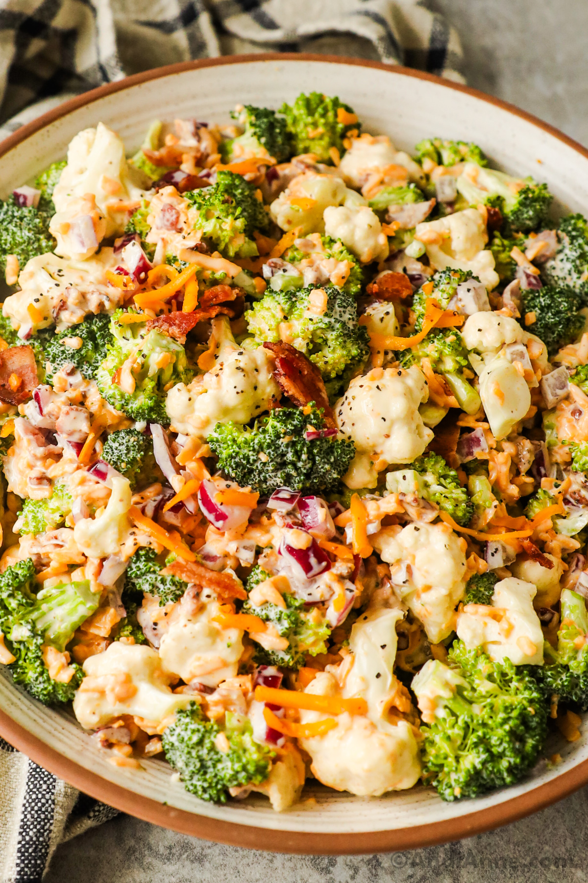 Close up of broccoli, cauliflower, crispy bacon, shredded cheese in a creamy dressing salad.