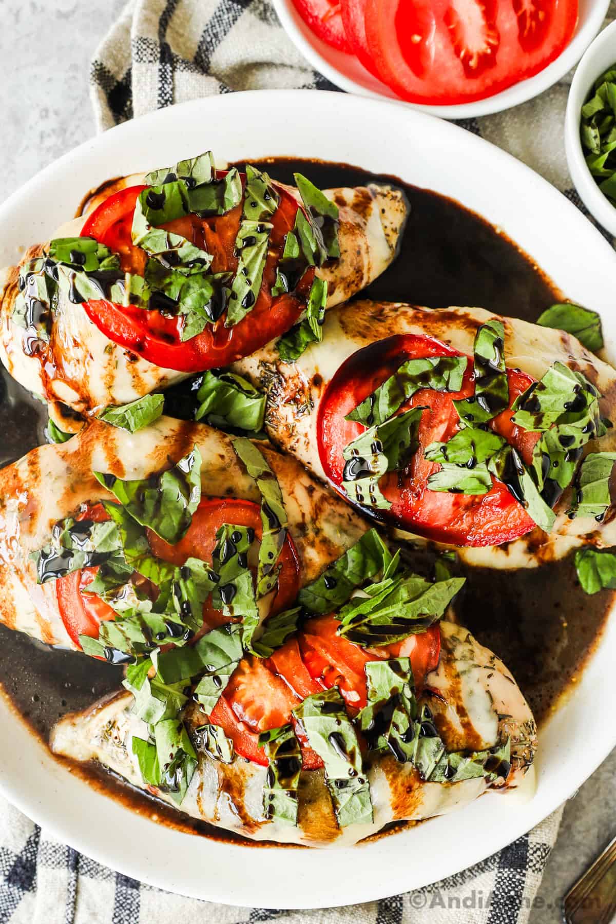 Four cooked chicken breasts covered in melted cheese, tomato slices, sliced fresh basil and drizzled with balsamic vinegar.