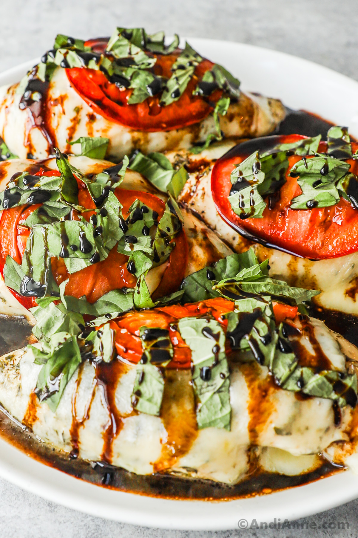 Close up of caprese chicken recipe with chicken breasts, sliced tomato, melted mozzarella, fresh basil and balsamic reduction drizzled on top