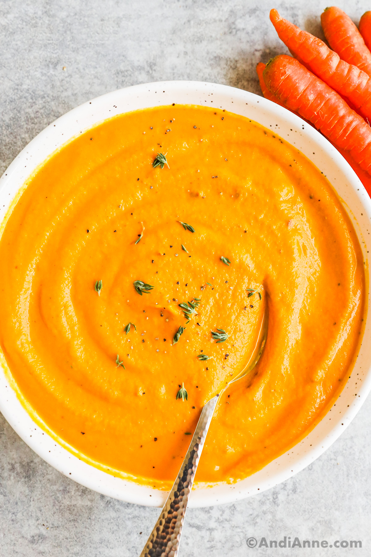 Close up of a bowl of creamy carrot soup with a spoon and a sprinkle of thyme