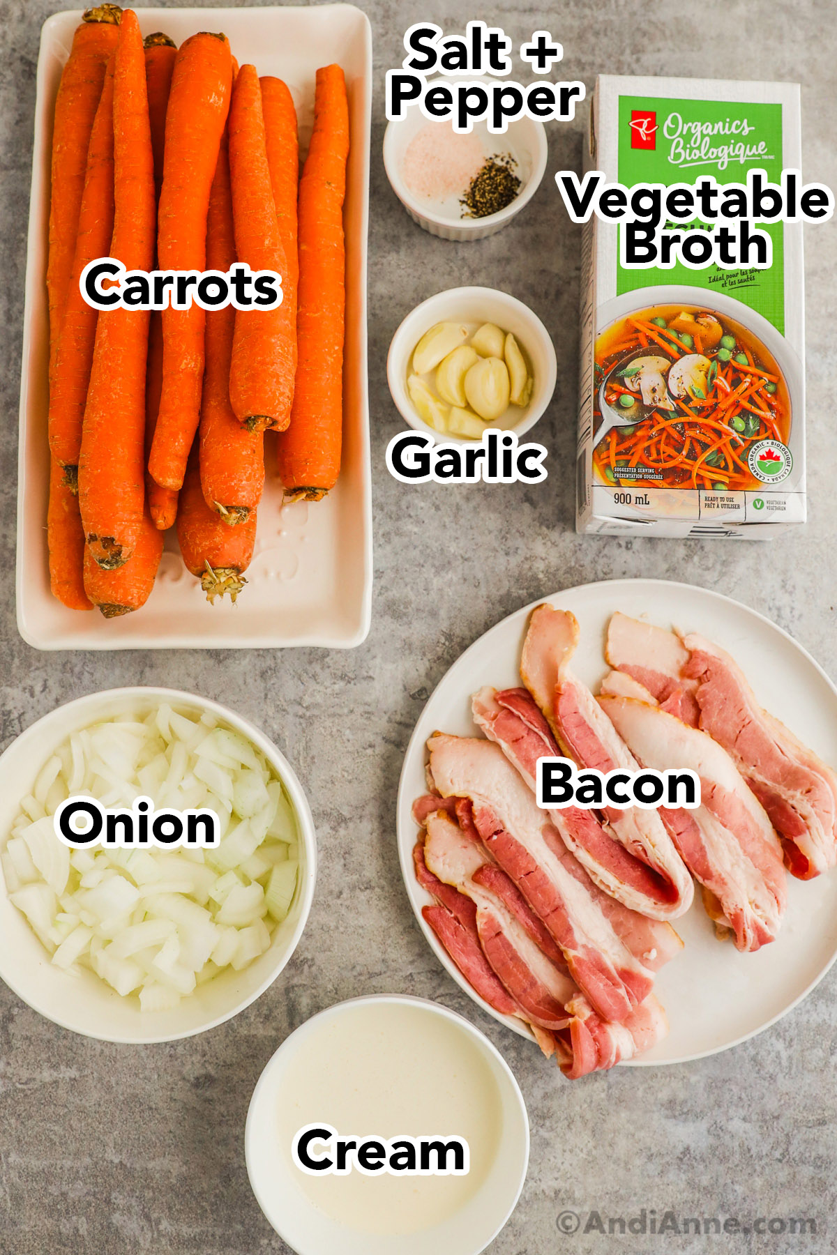 Recipe ingredients including carrots, bowls of salt and pepper, garlic cloves, chopped onion, raw bacon slices, cream and a carton of broth.