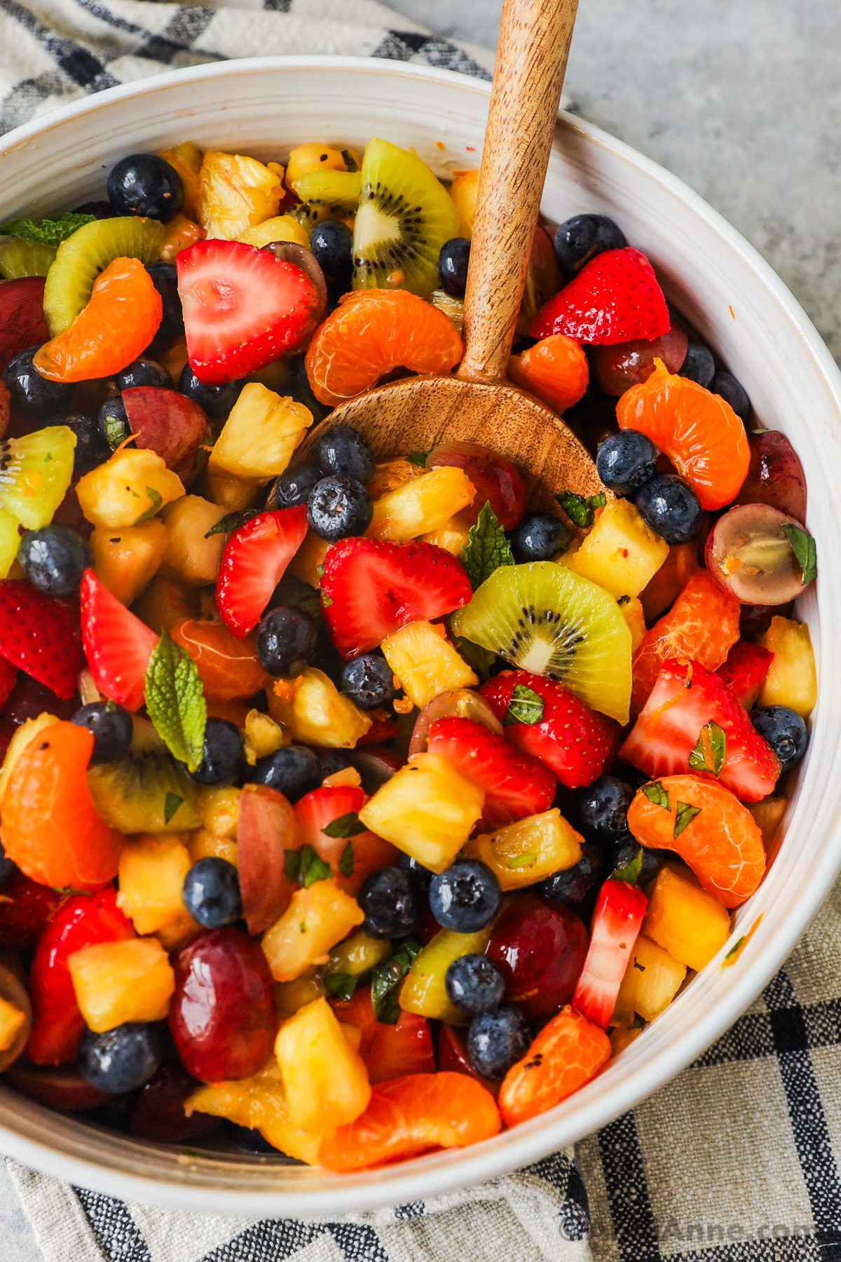 A wood spoon inside a bowl of fruit salad.