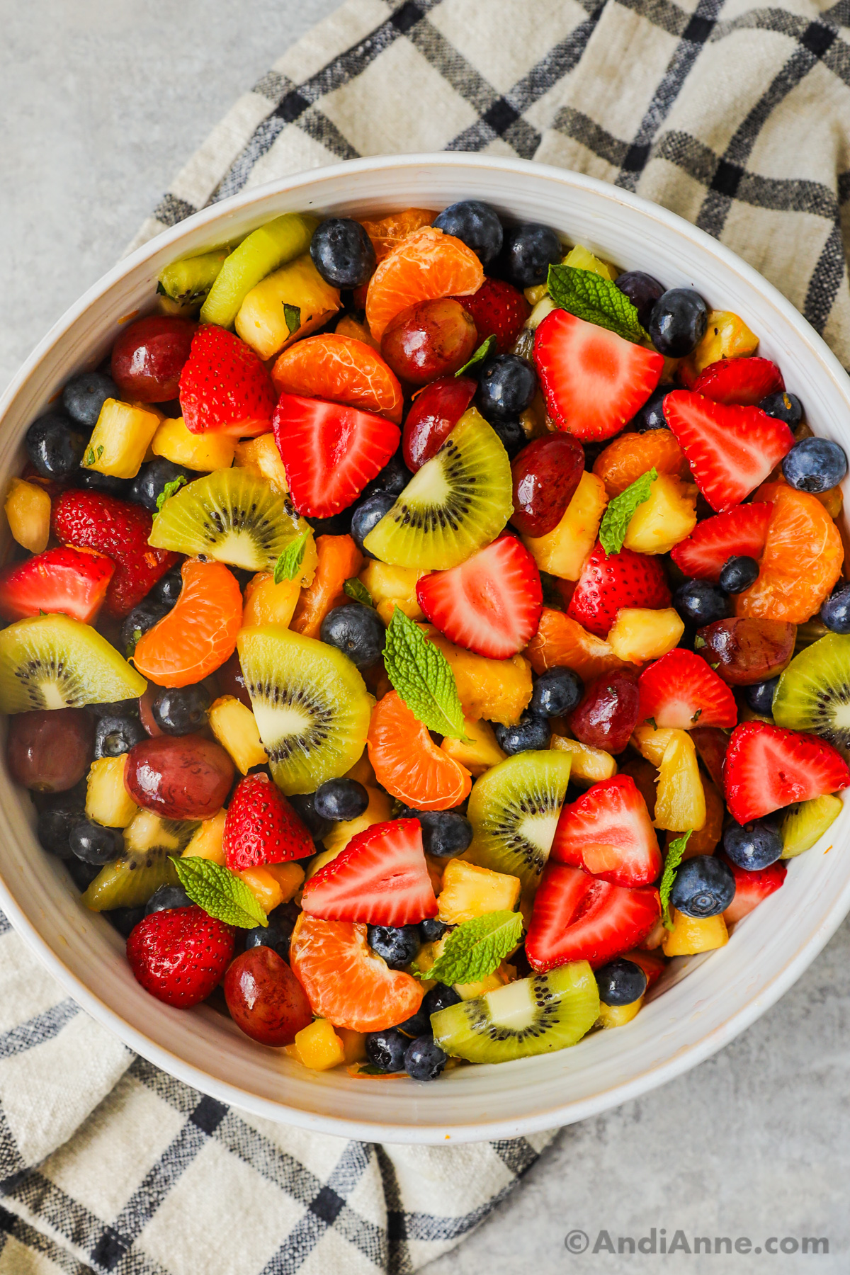 A large bowl filled with brightly colored fruit in a fruit salad with mint leaf garnishes.