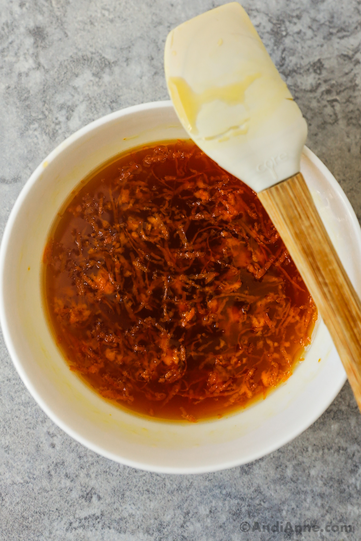 A bowl of brown liquid with orange zest and a small spatula.