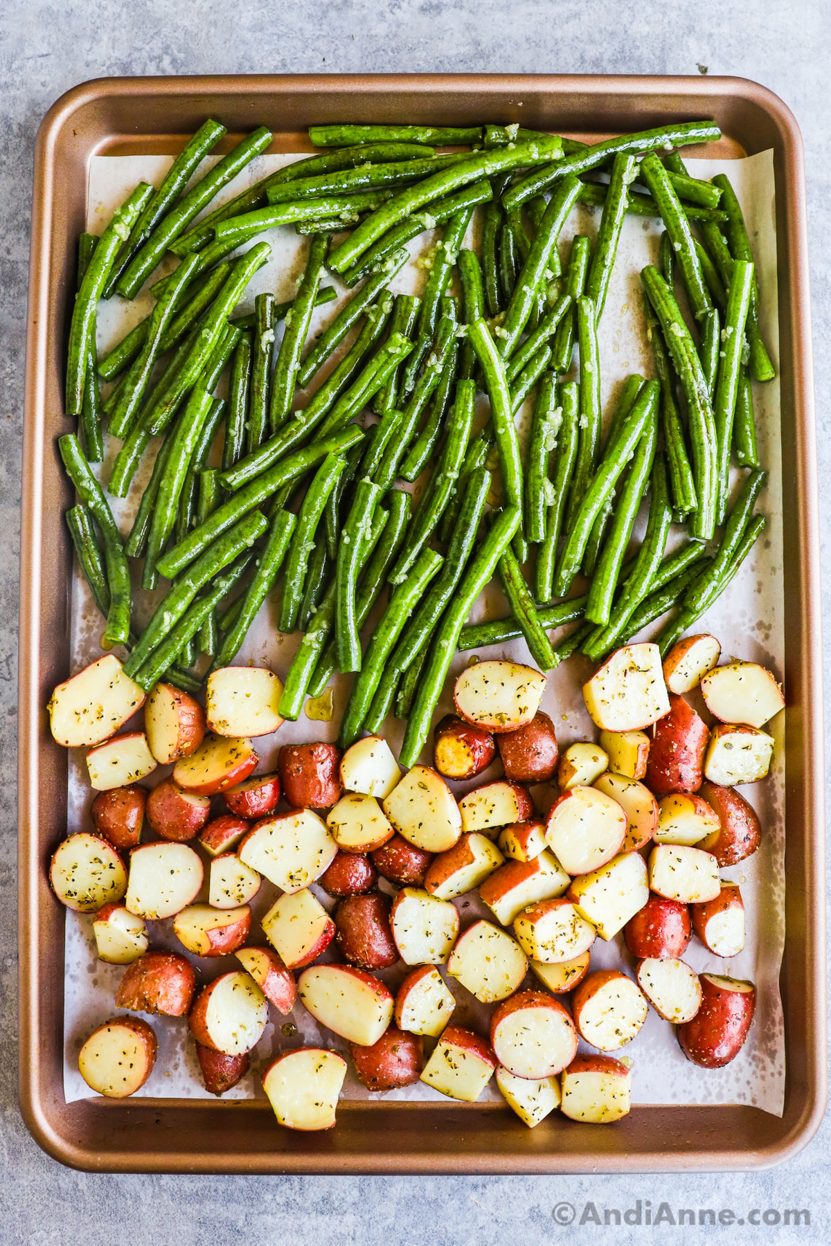 A sheet pan with uncooked green beans on the top half and slightly cooked sliced baby red potatoes on the bottom half.