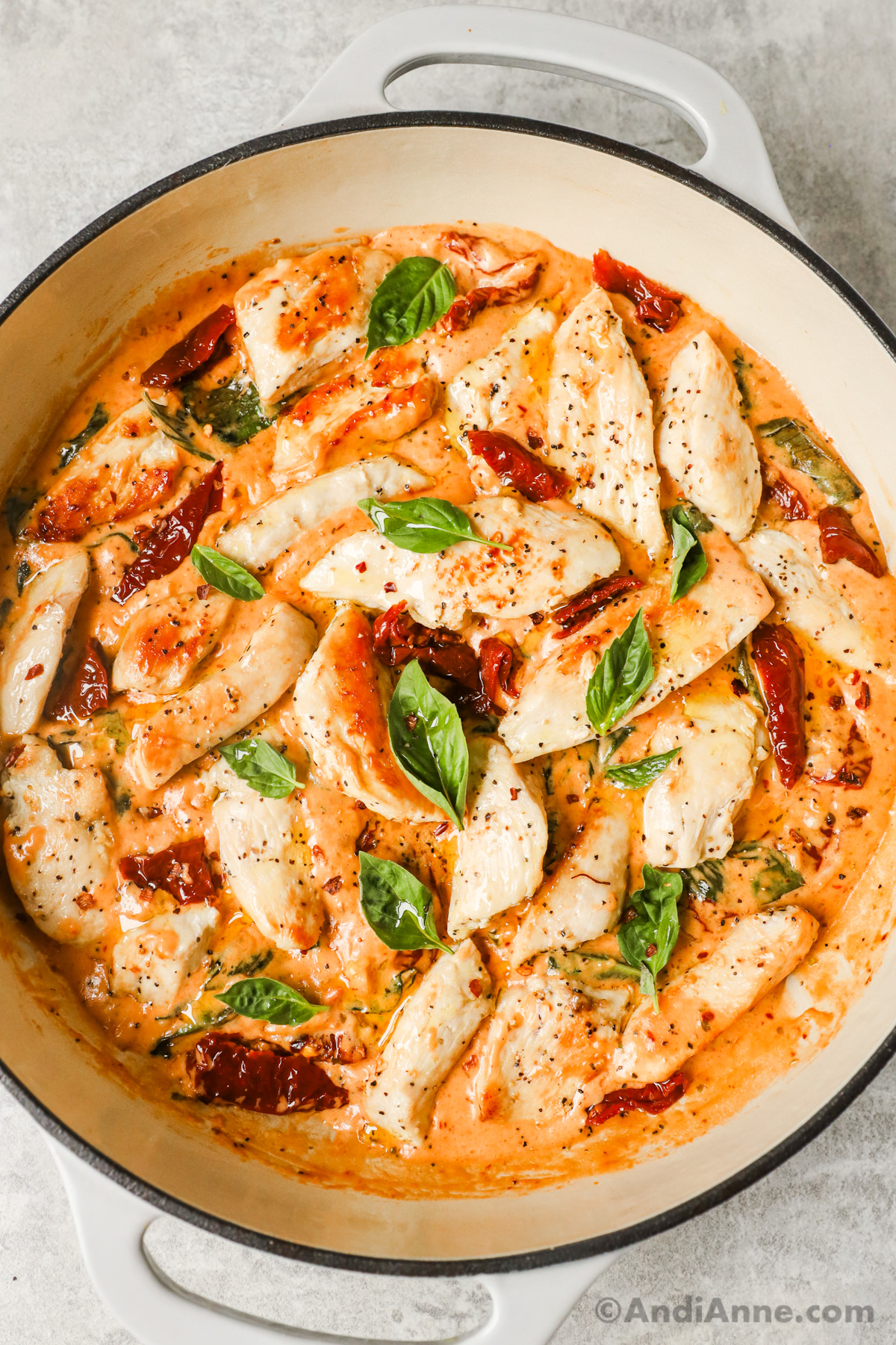 Close up of marry me chicken recipe with sliced chicken, sun dried tomatoes, and basil in a creamy sauce.