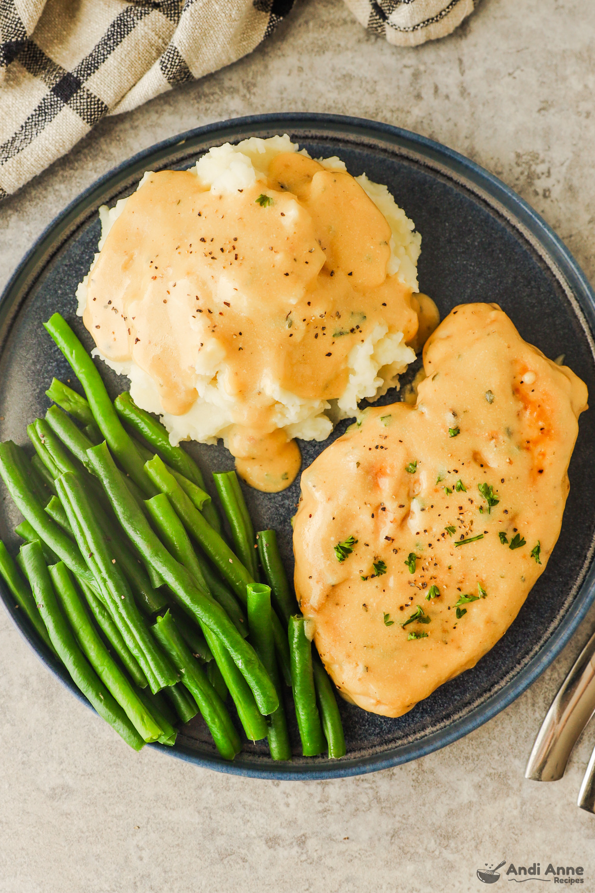 A plate with mashed potatoes drizzled with creamy ranch sauce, green beans, and a chicken breast with creamy sauce.