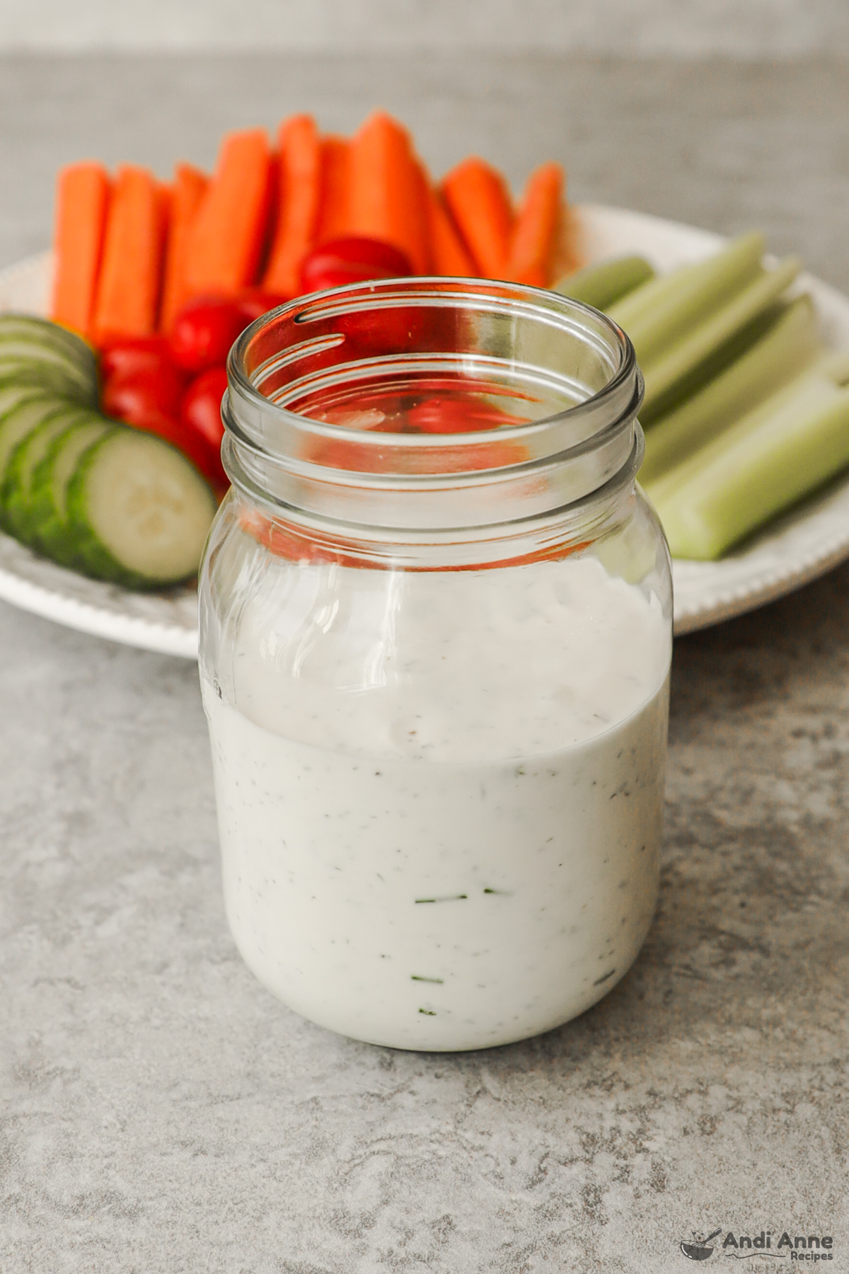 A jar of ranch dressing with chopped veggies on a plate in the background