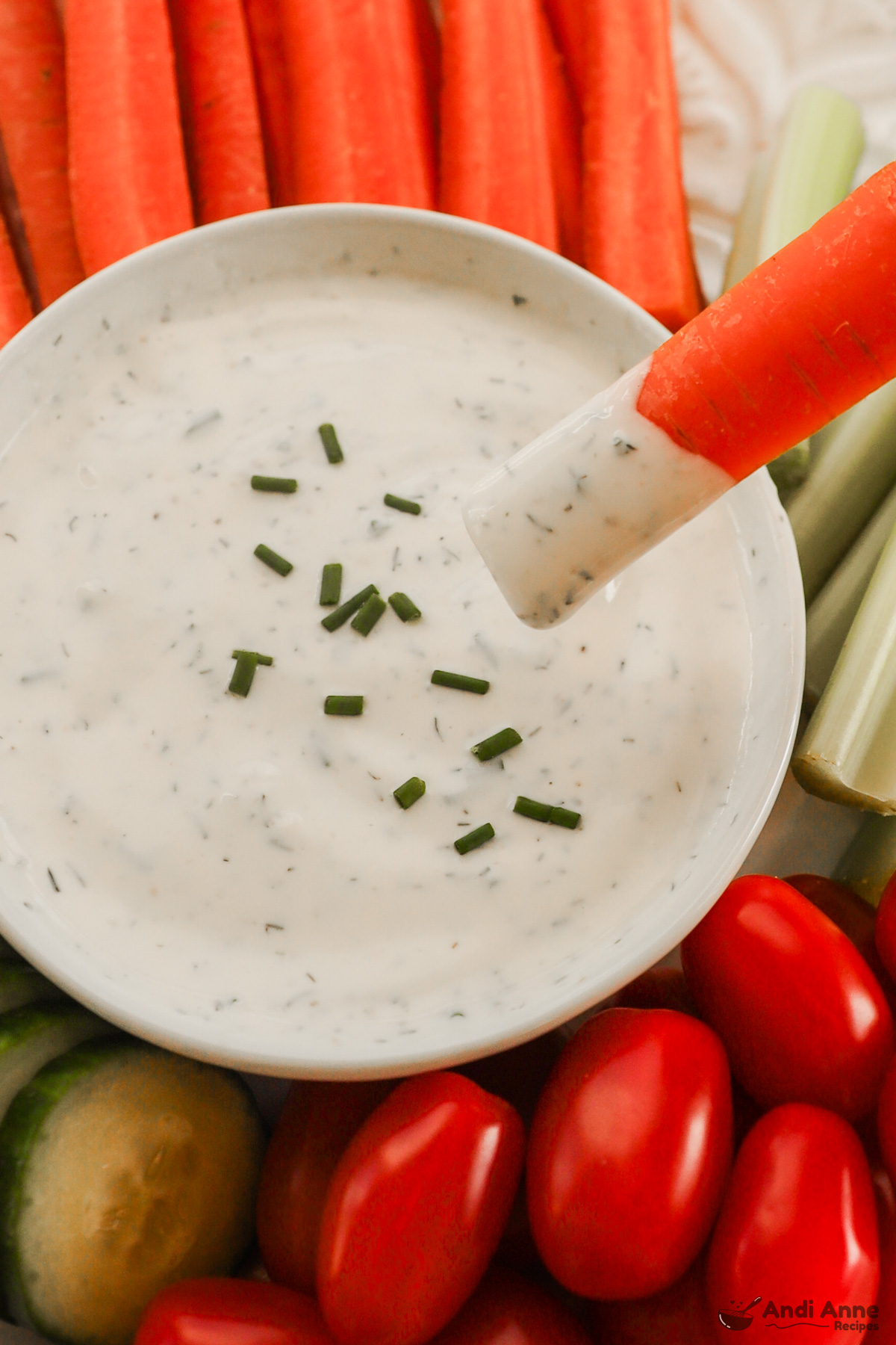 Close up of a bowl of ranch dressing with a carrot stick that has been dipped in