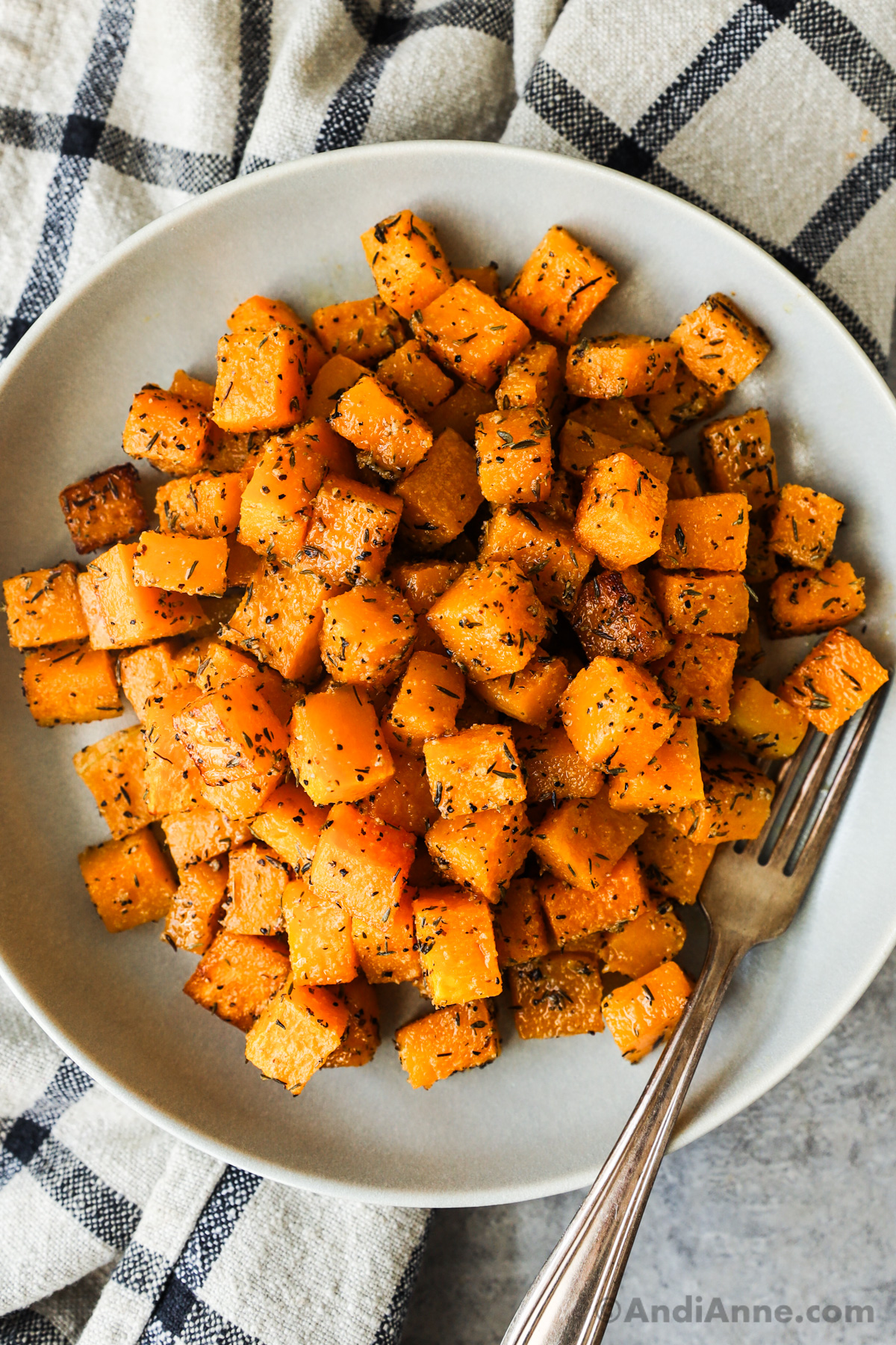 A plate of roasted cubed butternut squash with a fork