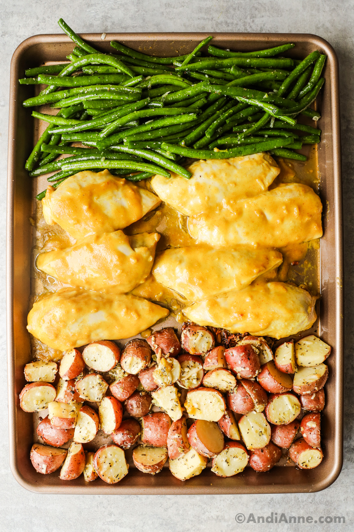 Baking sheet of potatoes, chicken breasts and green beans not fully cooked yet.