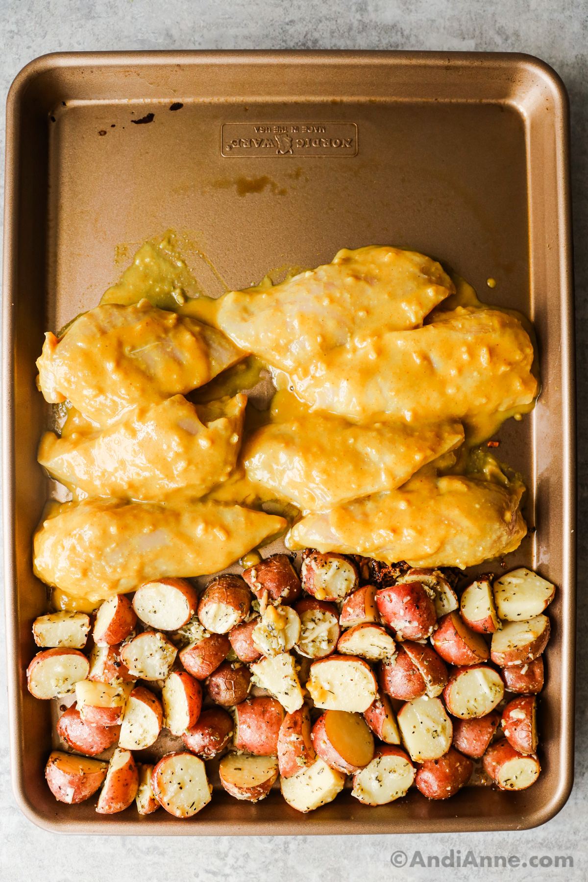 Baking sheet with sliced potatoes and sliced chicken breasts with honey mustard sauce.