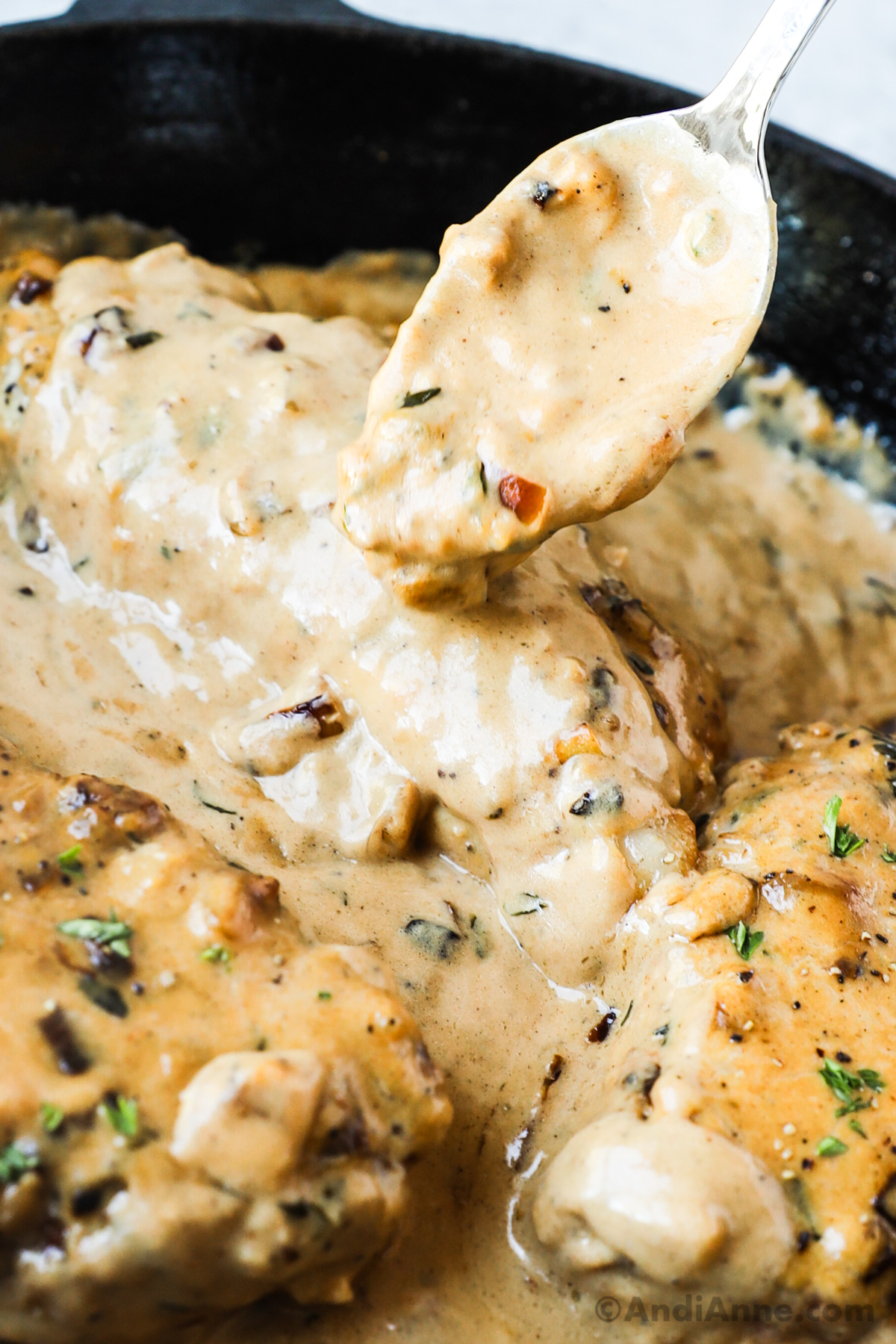 Close up of a spoon pouring gravy onto a smothered pork chop with gravy.