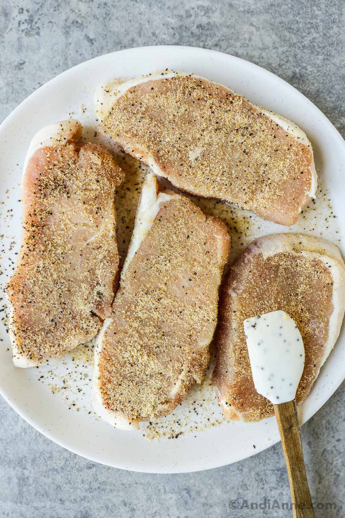 A plate of seasoned raw pork chops and a small spatula.