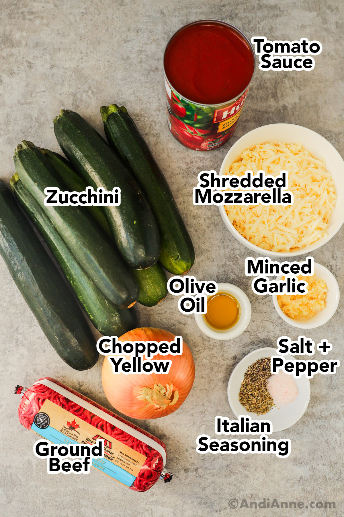 Zucchinis, can of tomato sauce, shredded mozzarella in bowl, bowls of mince garlic, olive oil, spices, a yellow onion and tube of ground beef.