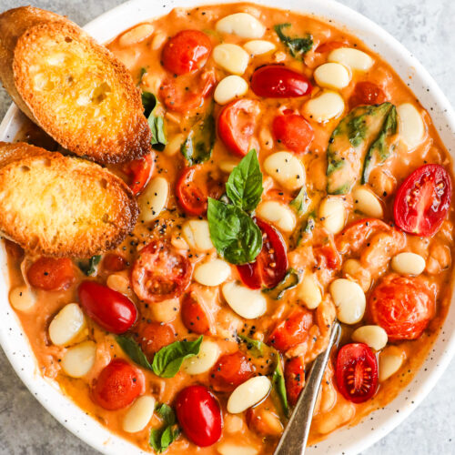 A bowl of tomato basil butter beans with two crusty baguette slices.