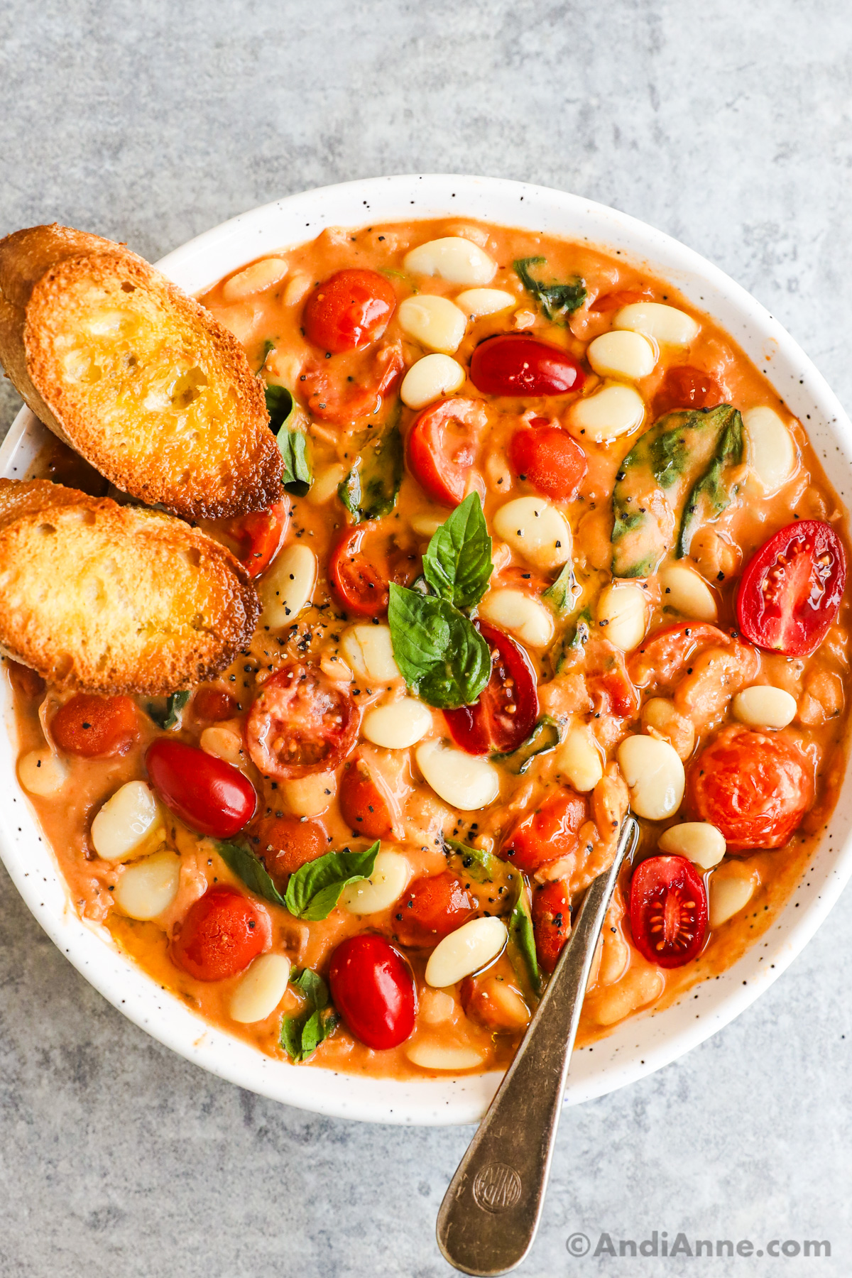 A bowl of tomato basil butter beans with two crusty baguette slices.