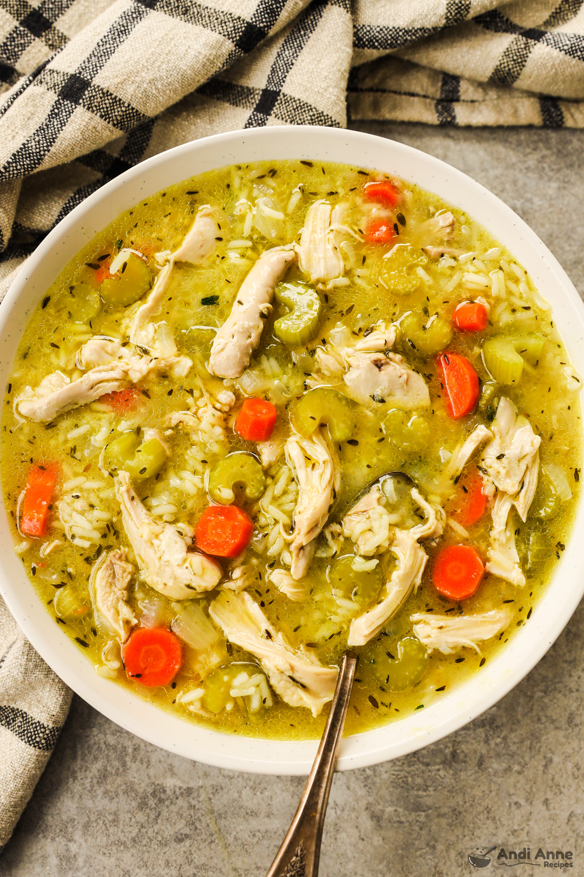 A bowl of chicken rice soup with chunks of chicken, rice, celery and carrots all in an broth