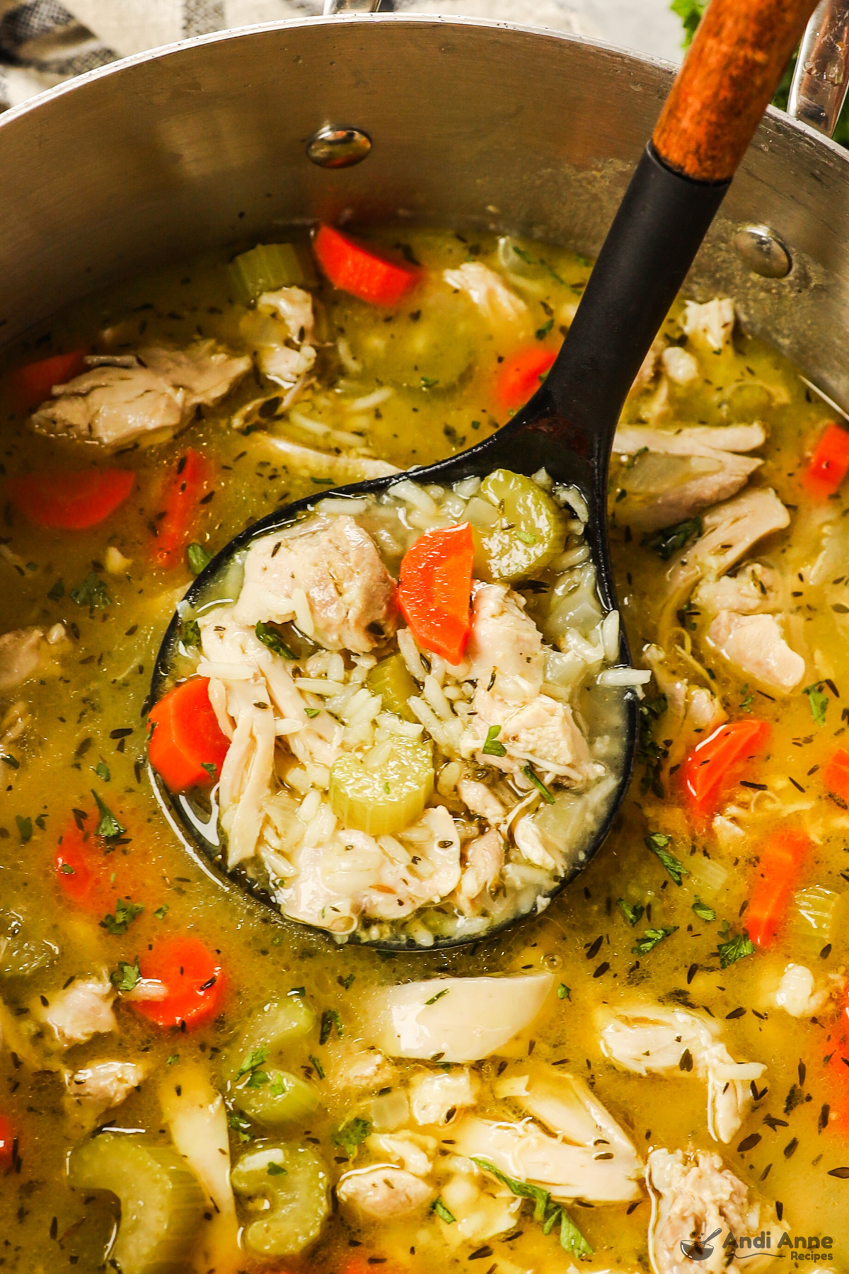 A soup ladle holding a scoop of chicken rice soup.