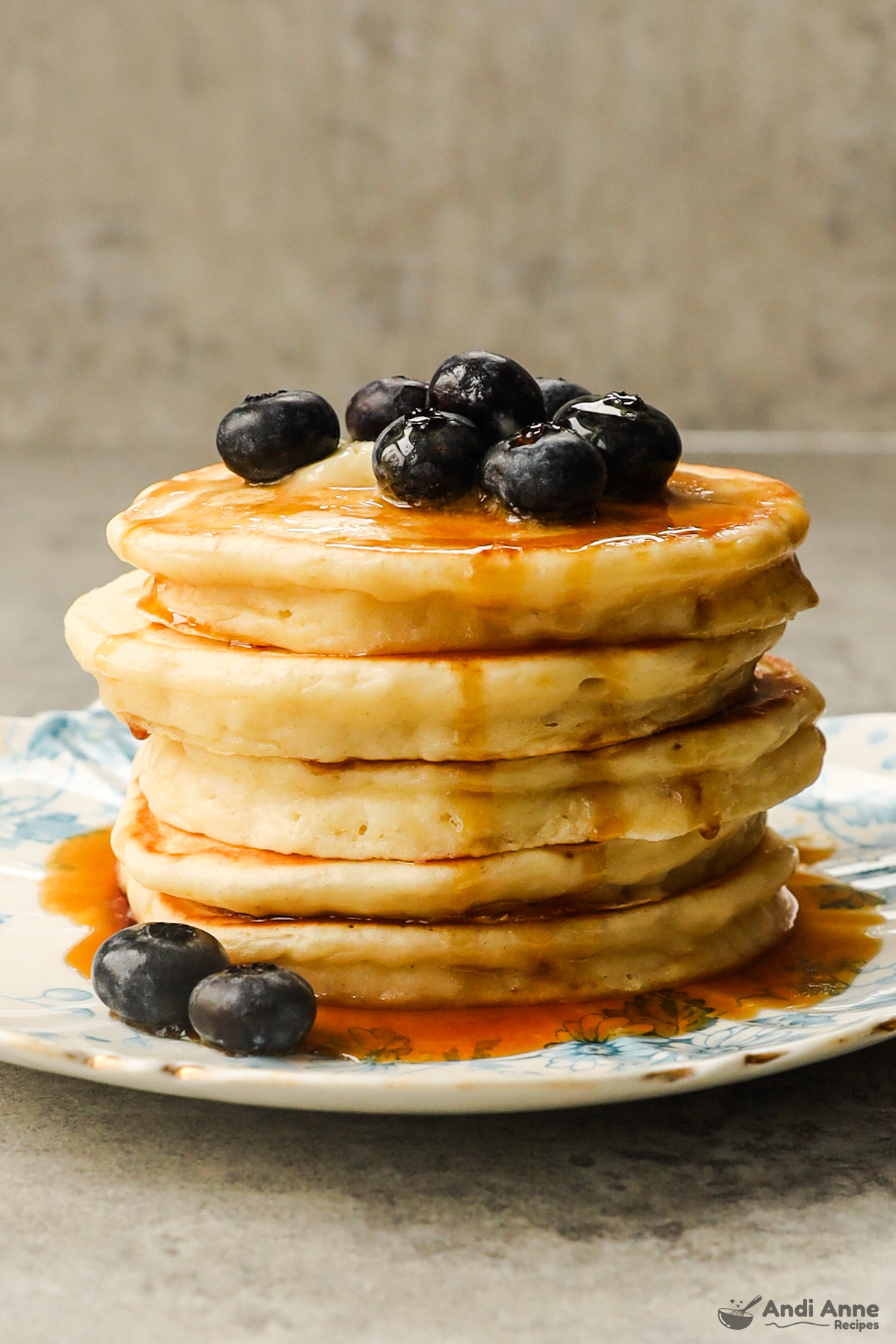 A stack of greek yogurt pancakes drizzled with maple syrup and topped with blueberries.