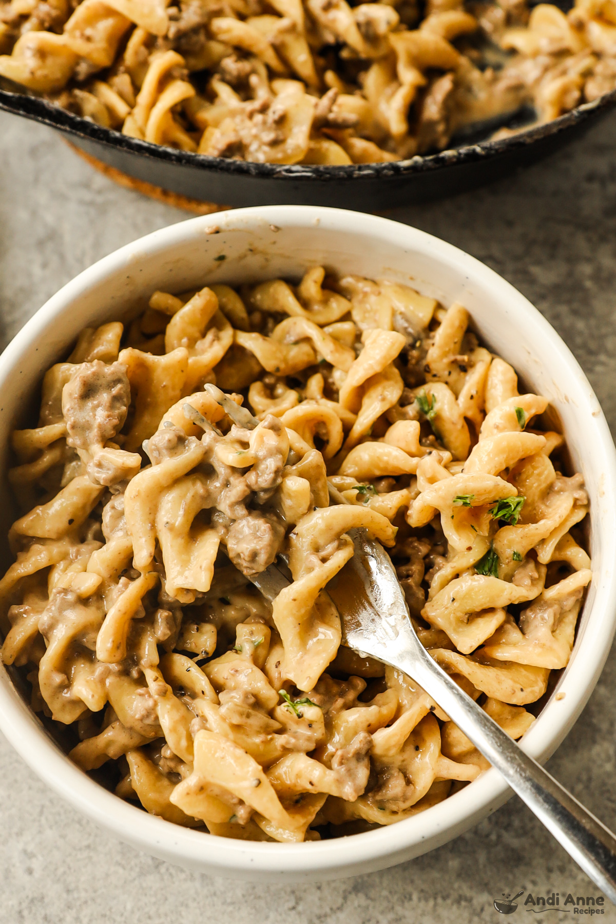 Bowl with ground beef stroganoff and a fork and pan beside it.