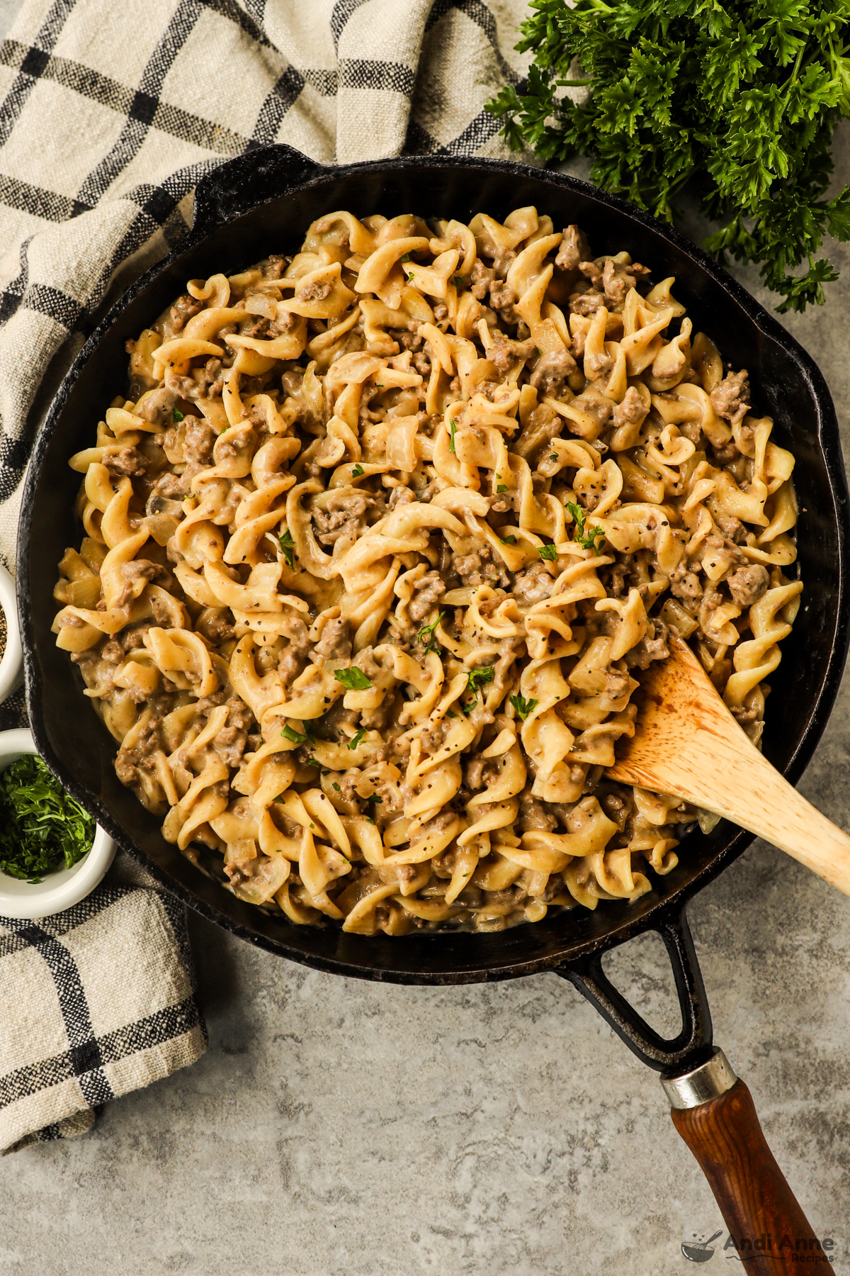 A skillet with ground beef stroganoff and a wood spoon