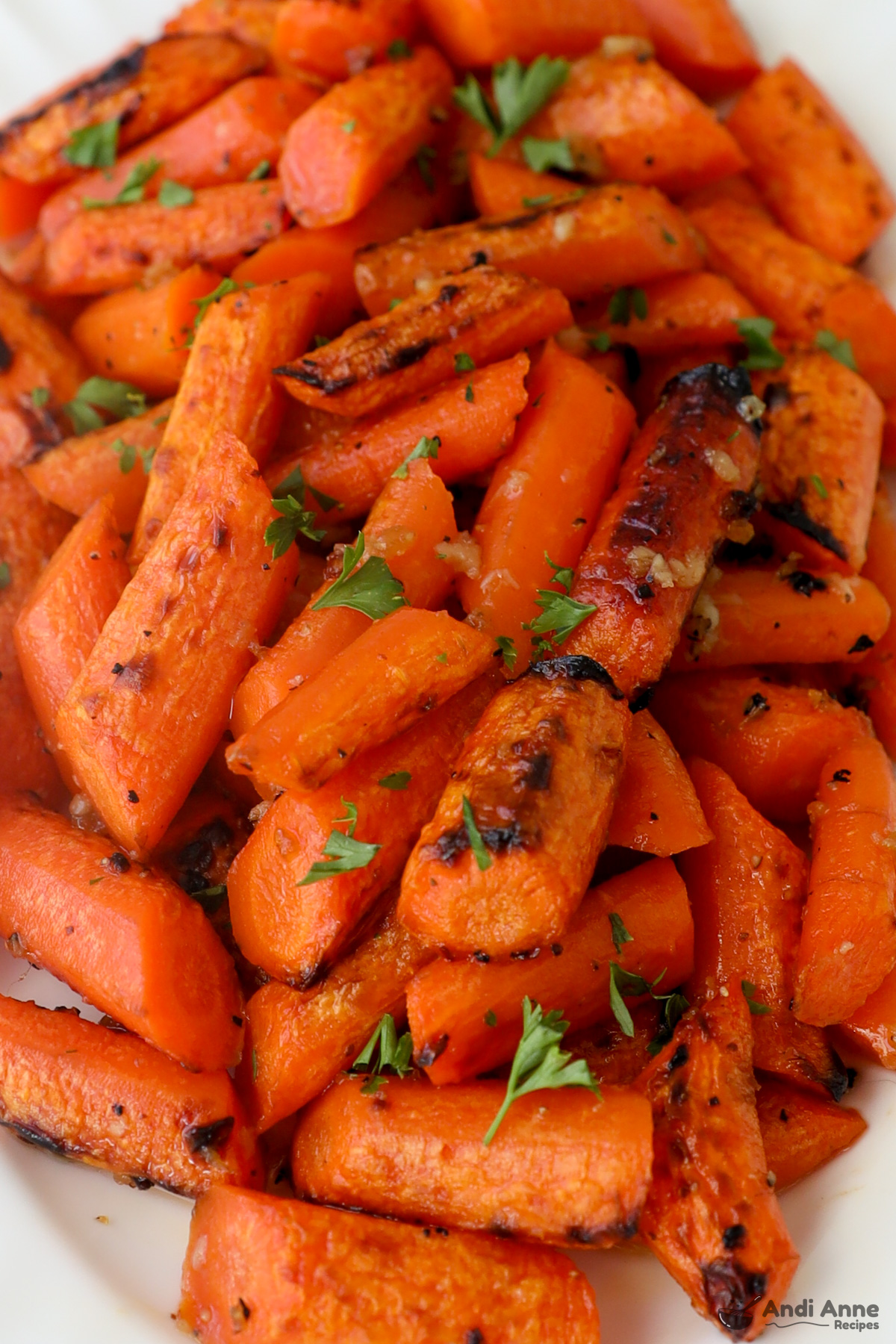 Close up of chopped cooked carrots some charred, with a spinkle of garlic and fresh parsley