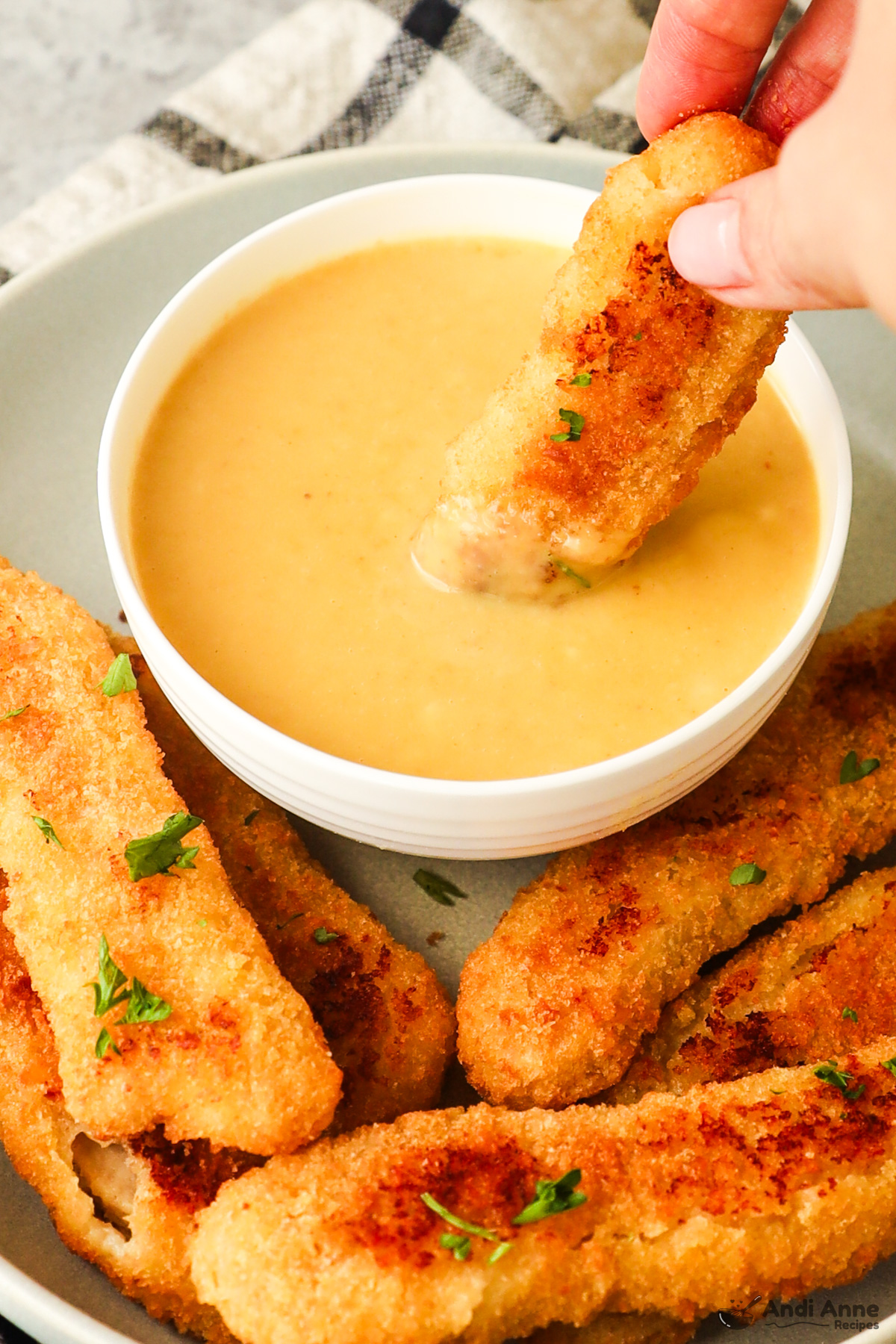 A bowl of honey mustard with chicken fingers in front.