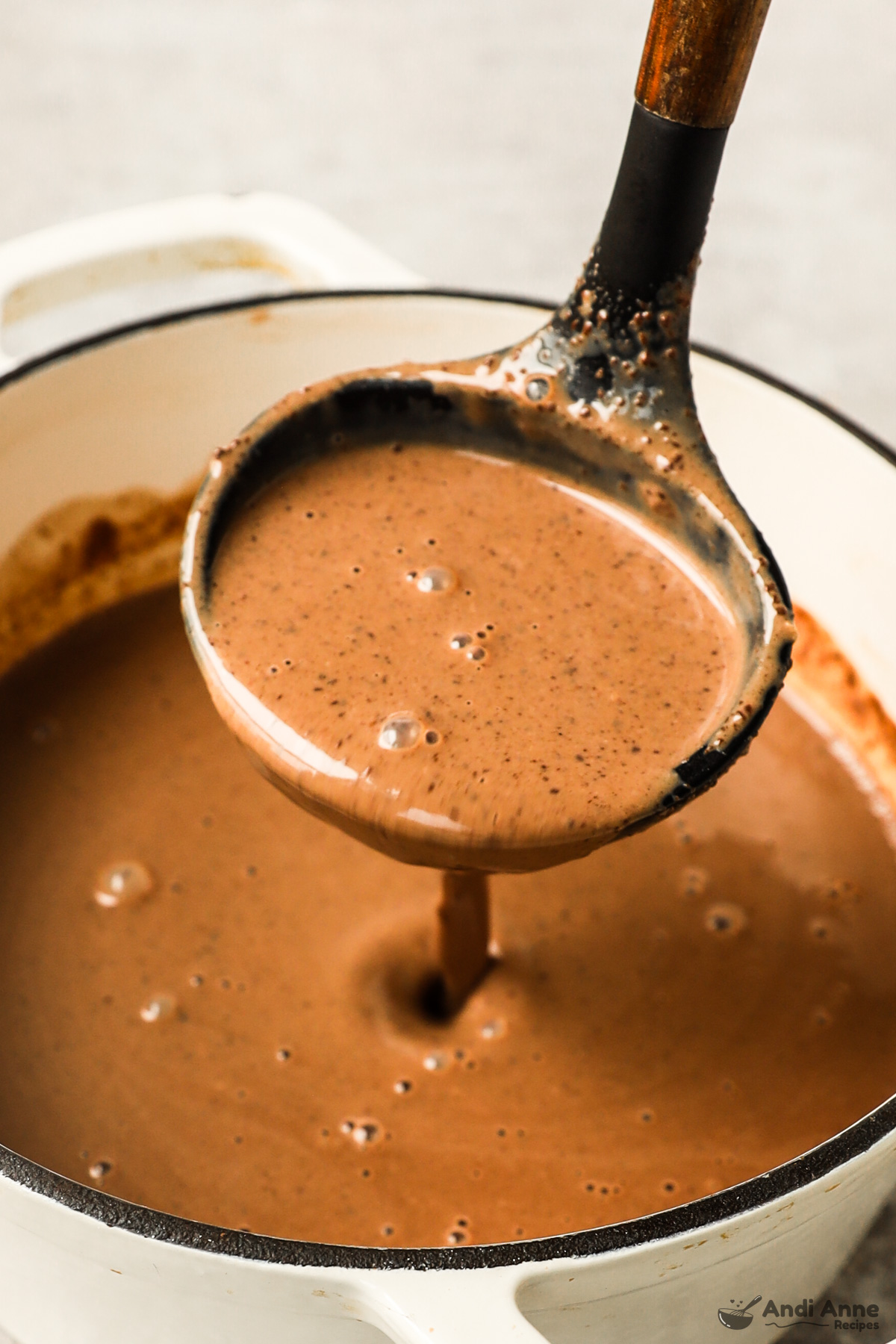 A ladle scooping a cup of hot chocolate from a pot.