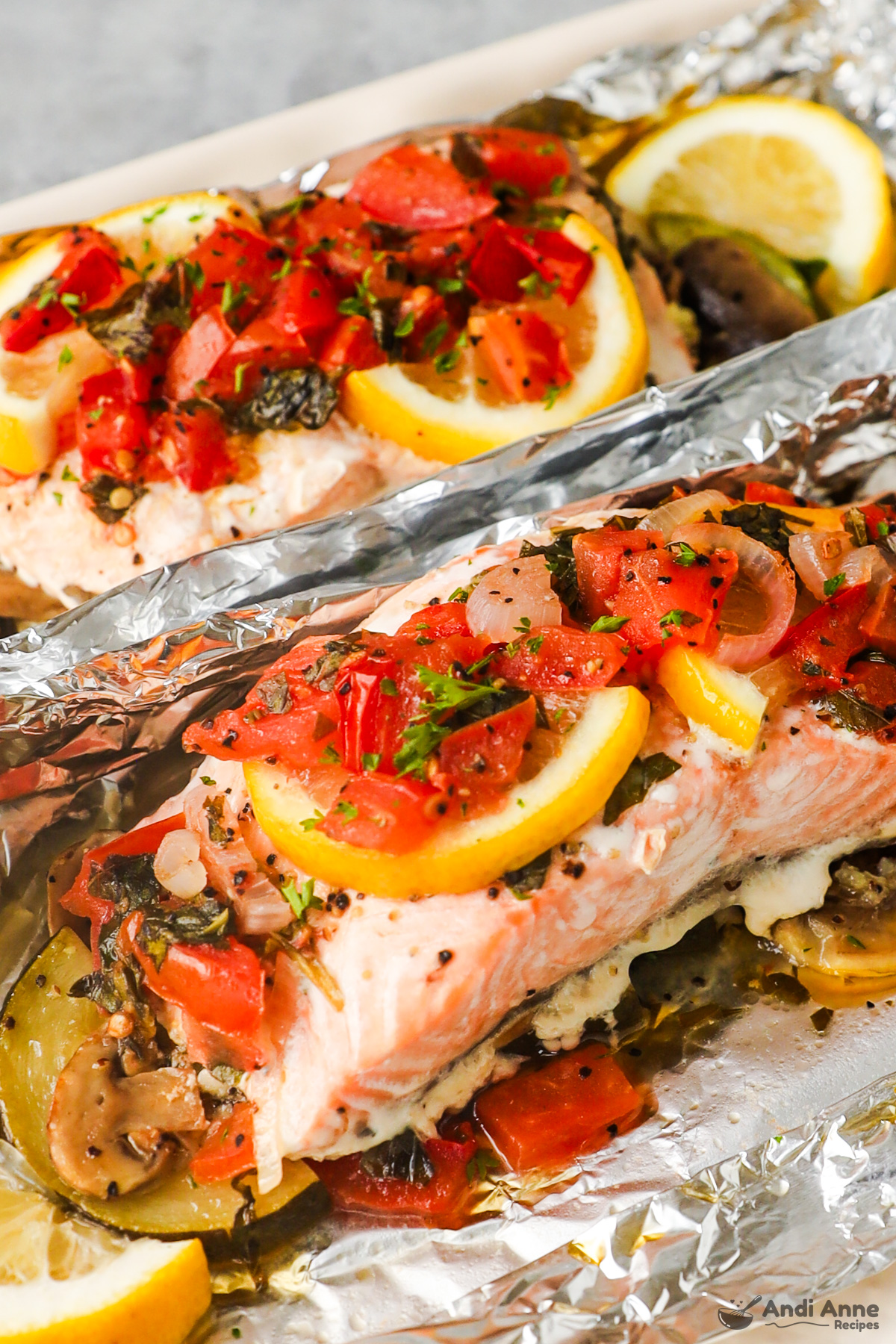 Close up of tomato salsa, lemon slices and salmon fillets all wrapped in foil.