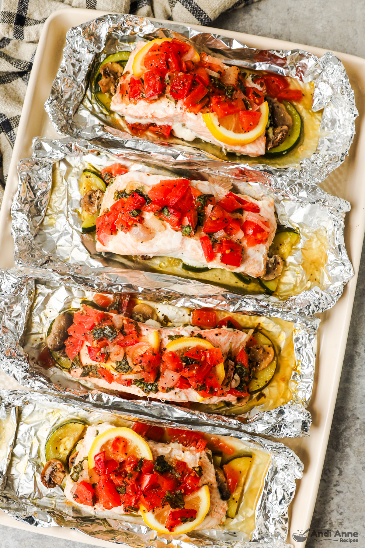 Four salmon foil packets with zucchini and tomato salsa on top.