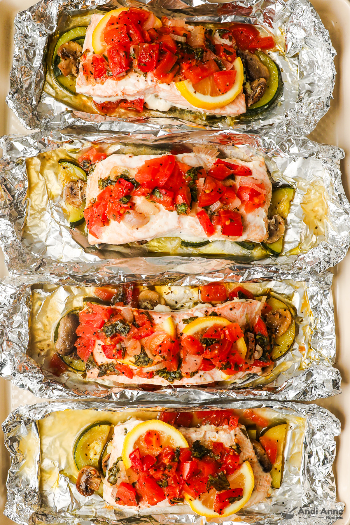 Four salmon foil packets with zucchini and tomato salsa on top.