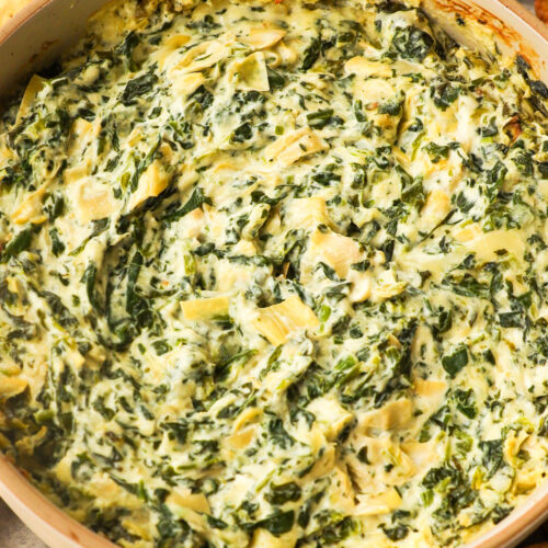 A round dish with spinach artichoke dip surrounded with crackers