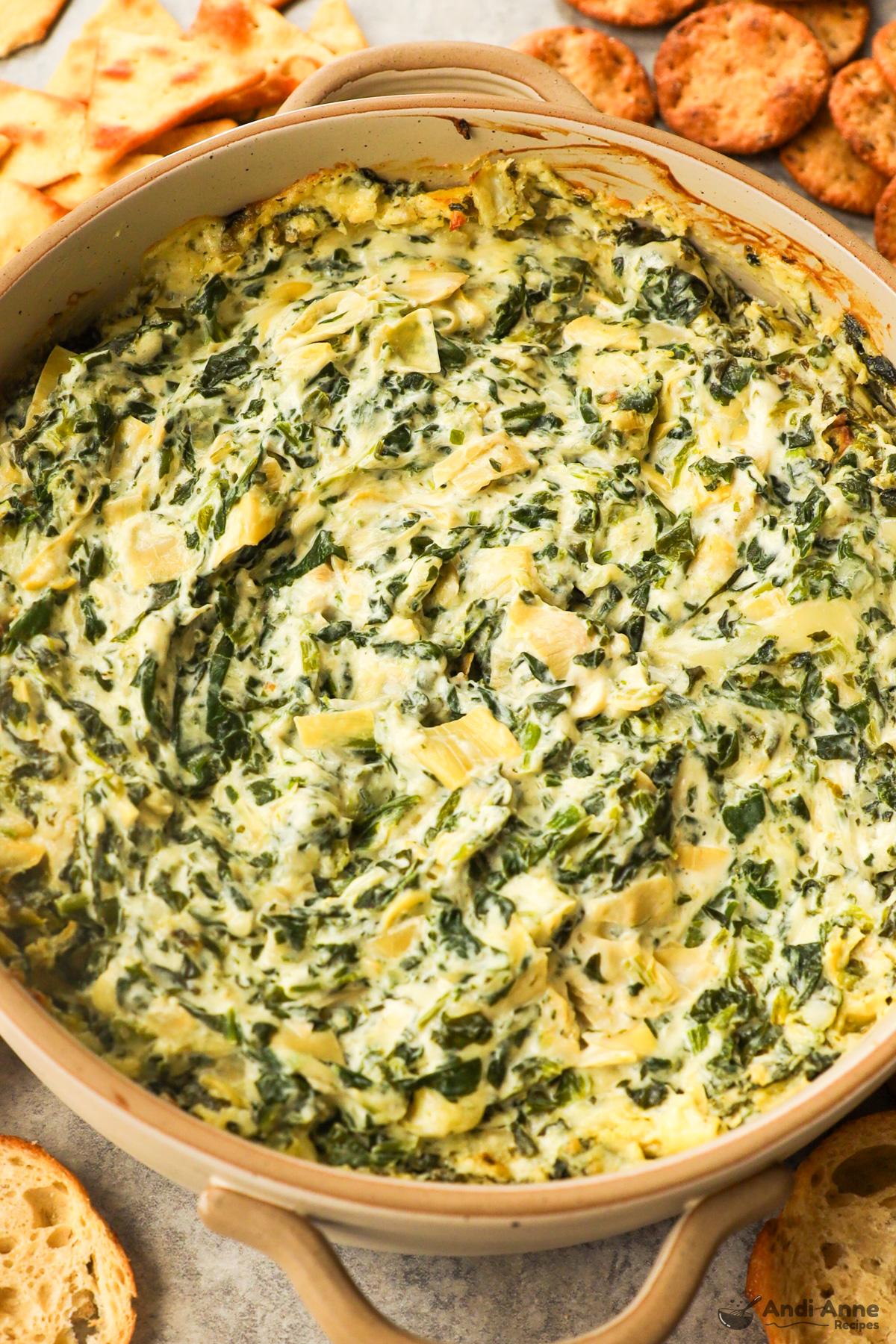 Round baking dish with spinach artichoke dip inside and crackers surrounding it.