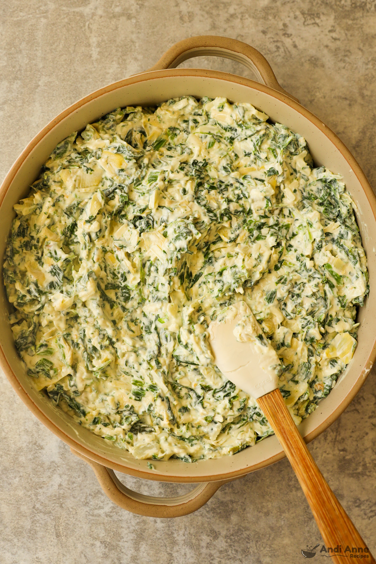 Round dish with spinach artichoke dip with a spatula.