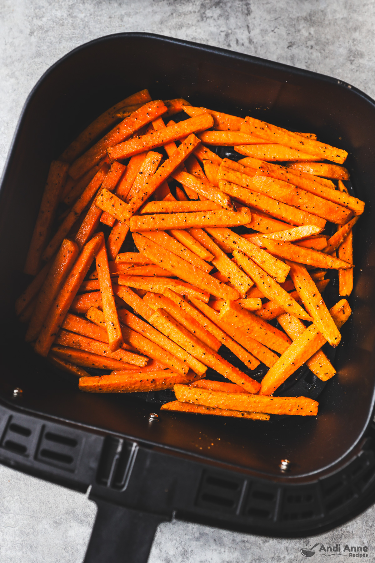 An air fryer basket with uncooked sweet potato fries inside