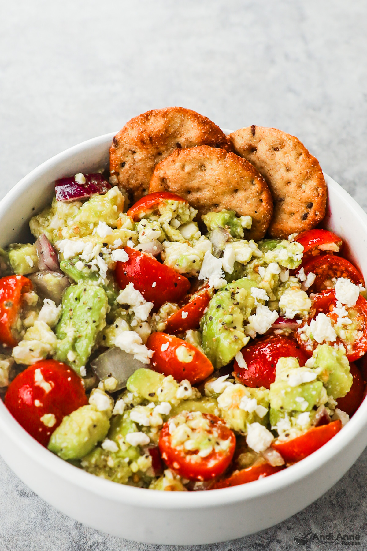 Bowl of avocado feta tomato dip with a few crackers on the side