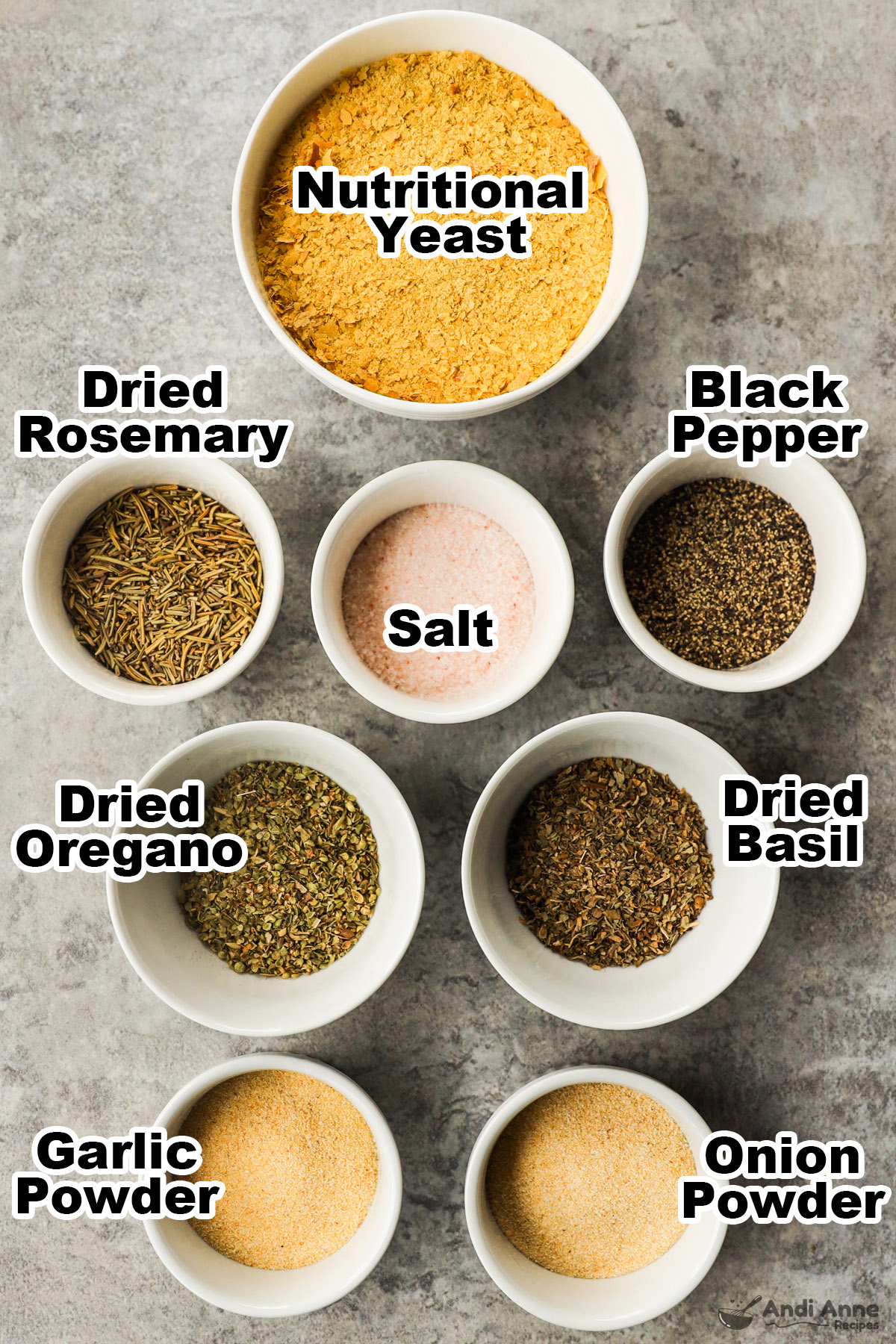 Various spices in bowls including dried roesemary, oregano, basil, salt and pepper and nutritional yeast