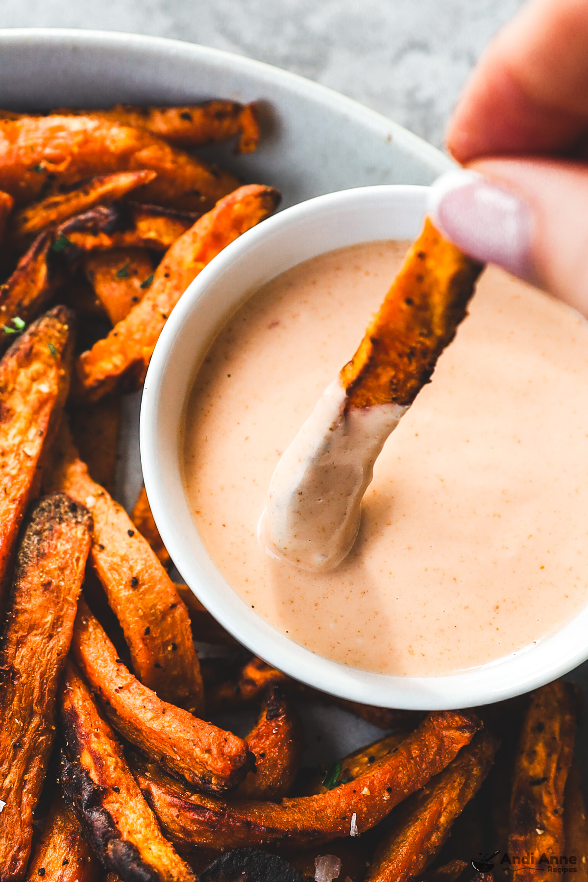 A fry being dipped into bowl of sauce with more fries surrounding on plate