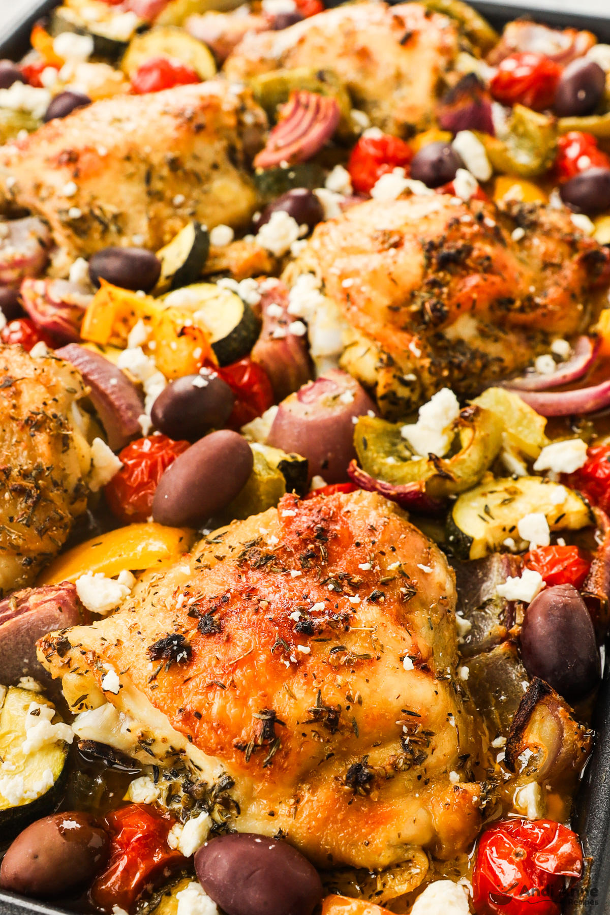 Close up of greek chicken thighs and veggies on a baking sheet