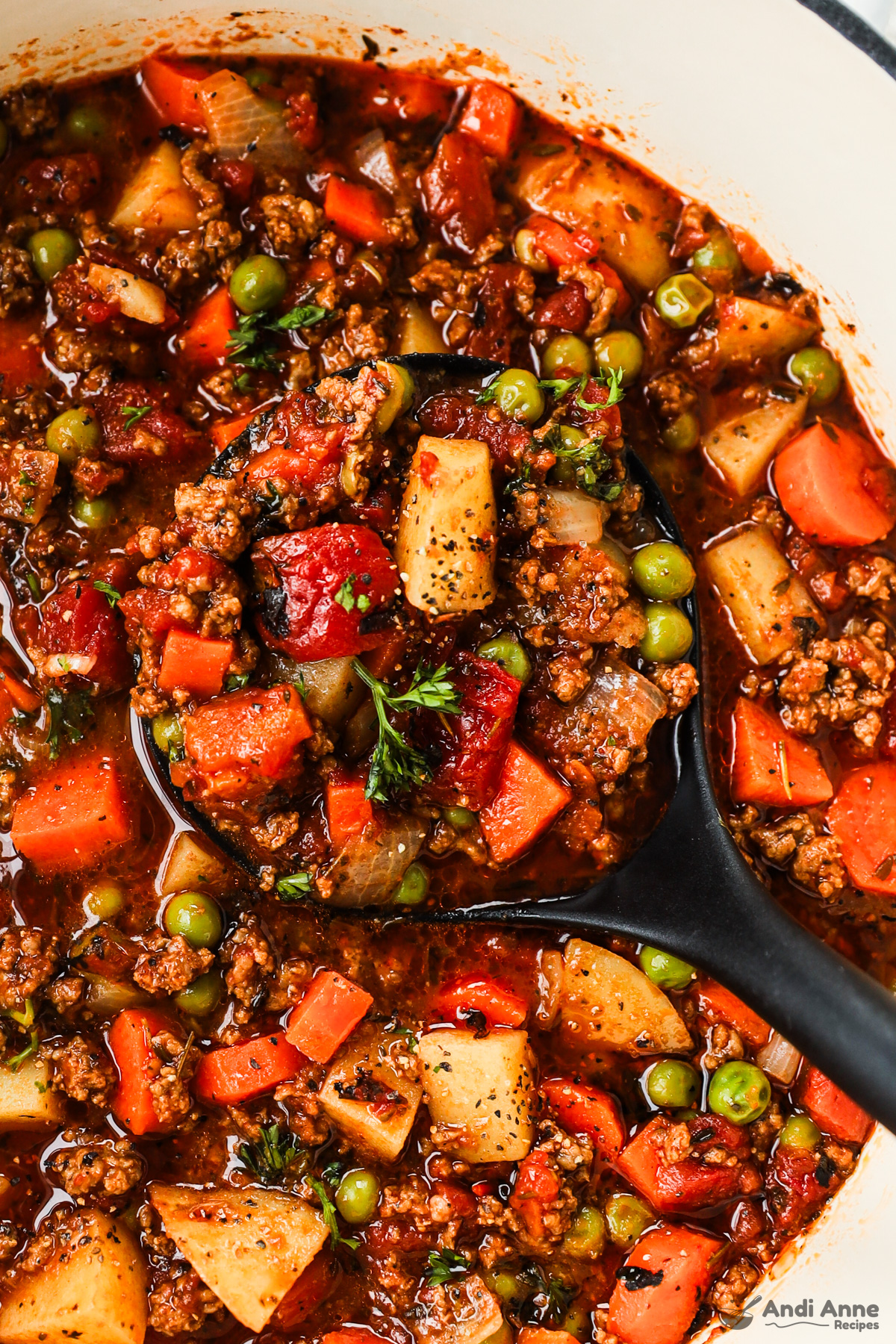 Close up of ground beef stew with chopped veggies and a soup ladle.