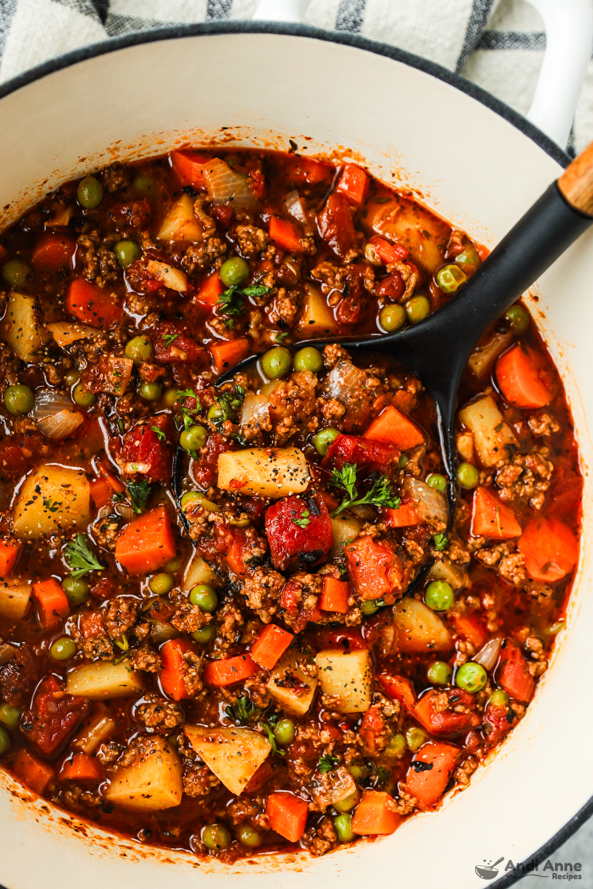 A pot of ground beef stew loaded with veggies and ground beef and a soup ladle