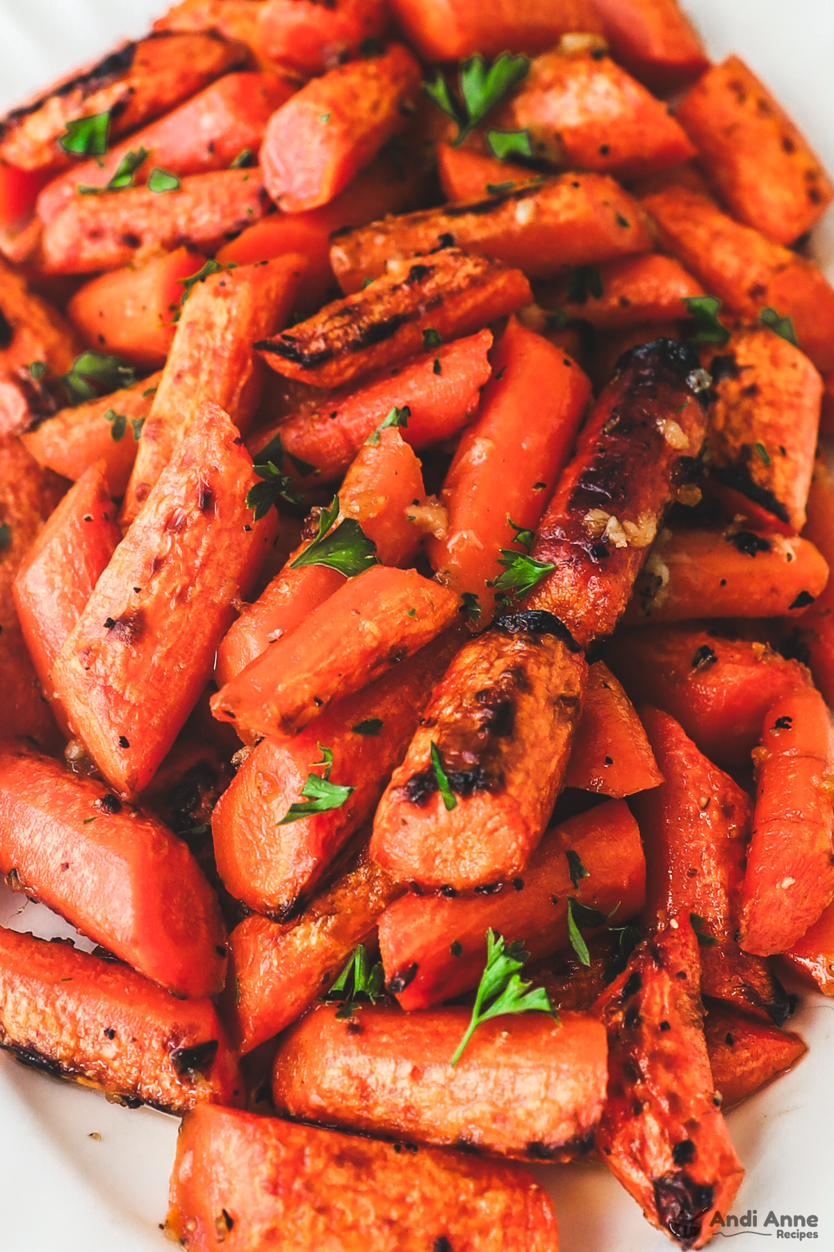 Close up of honey garlic butter carrots, some of them a little charred, with bits of parsley for garnish