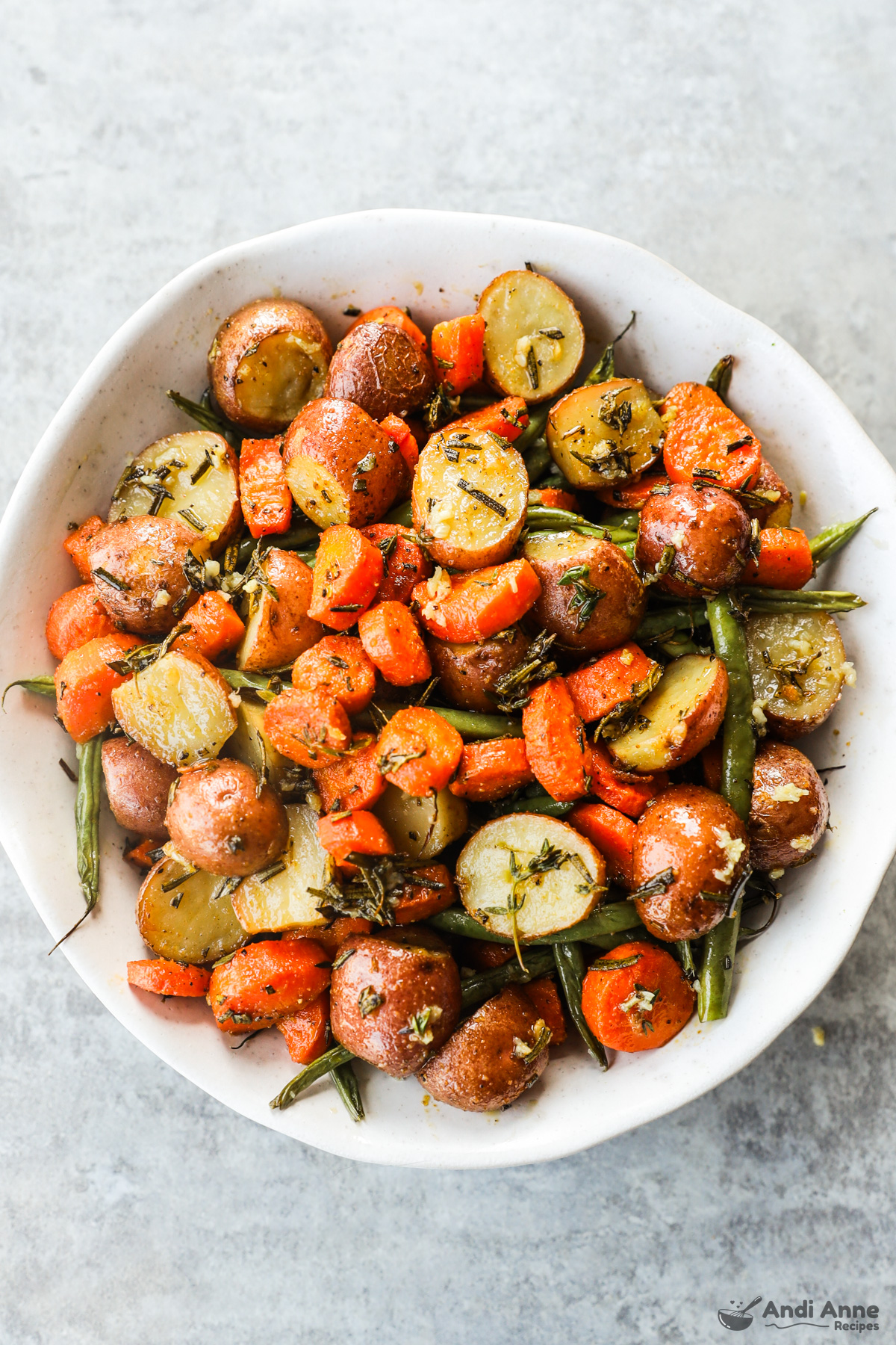 Bowl of roasted potatoes, carrots and green beans all mixed with herbs