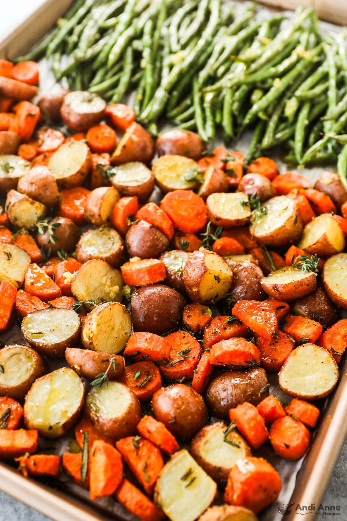 close up of chopped roasted potatoes and carrots on a baking sheet with green beans in background