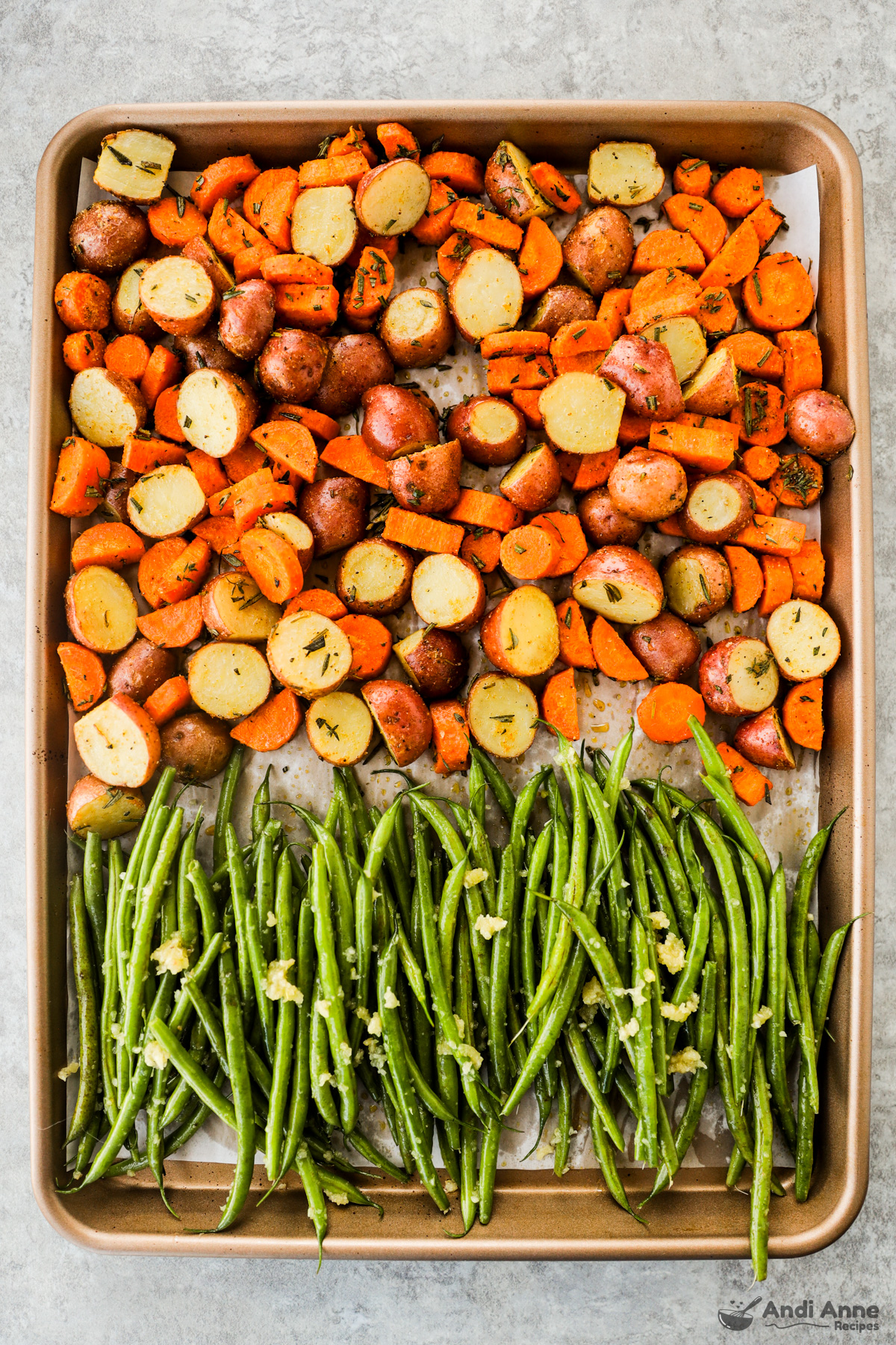 A sheet pan with potatoes and carrots on one half and green beans on the other half