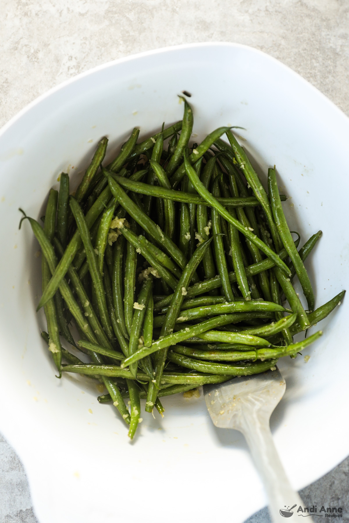 A bowl of green beans tossed with oil and minced garlic.