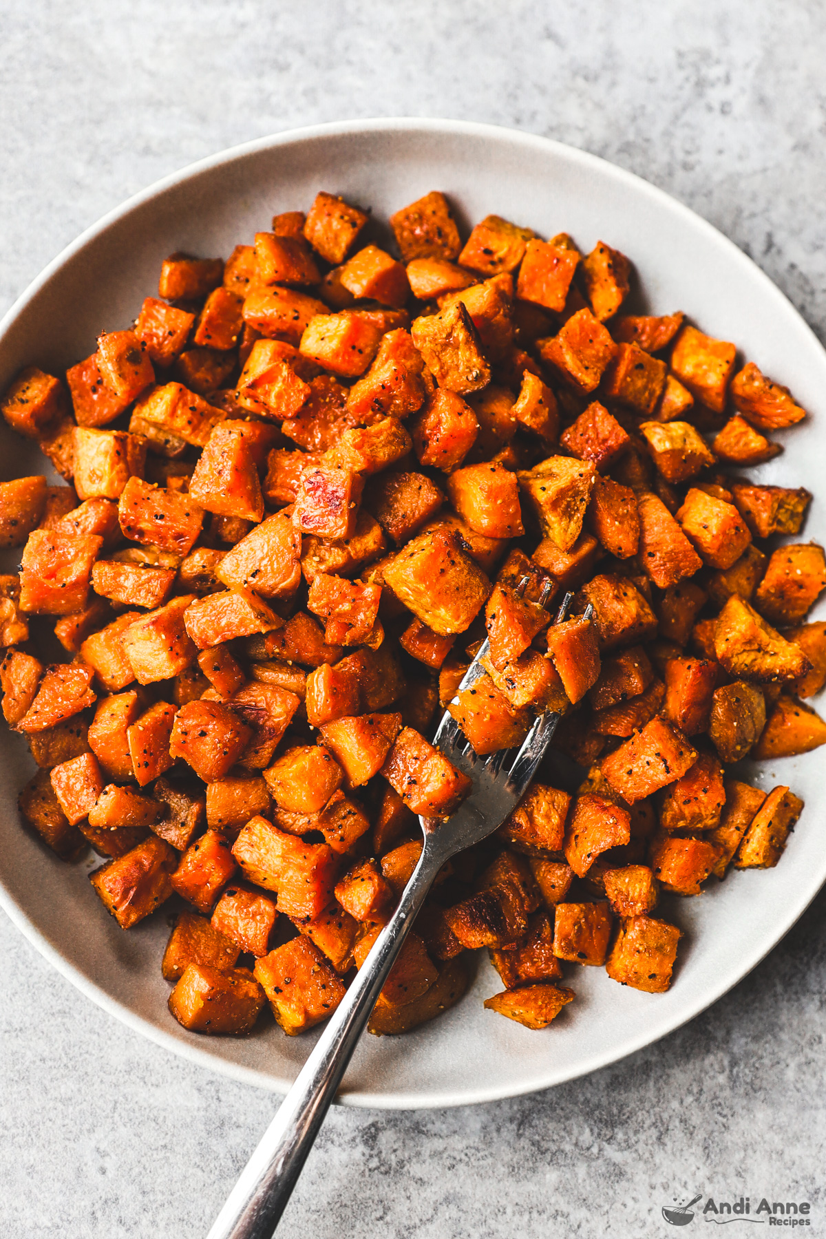 A plate of cooked cubed sweet potatoes with a fork