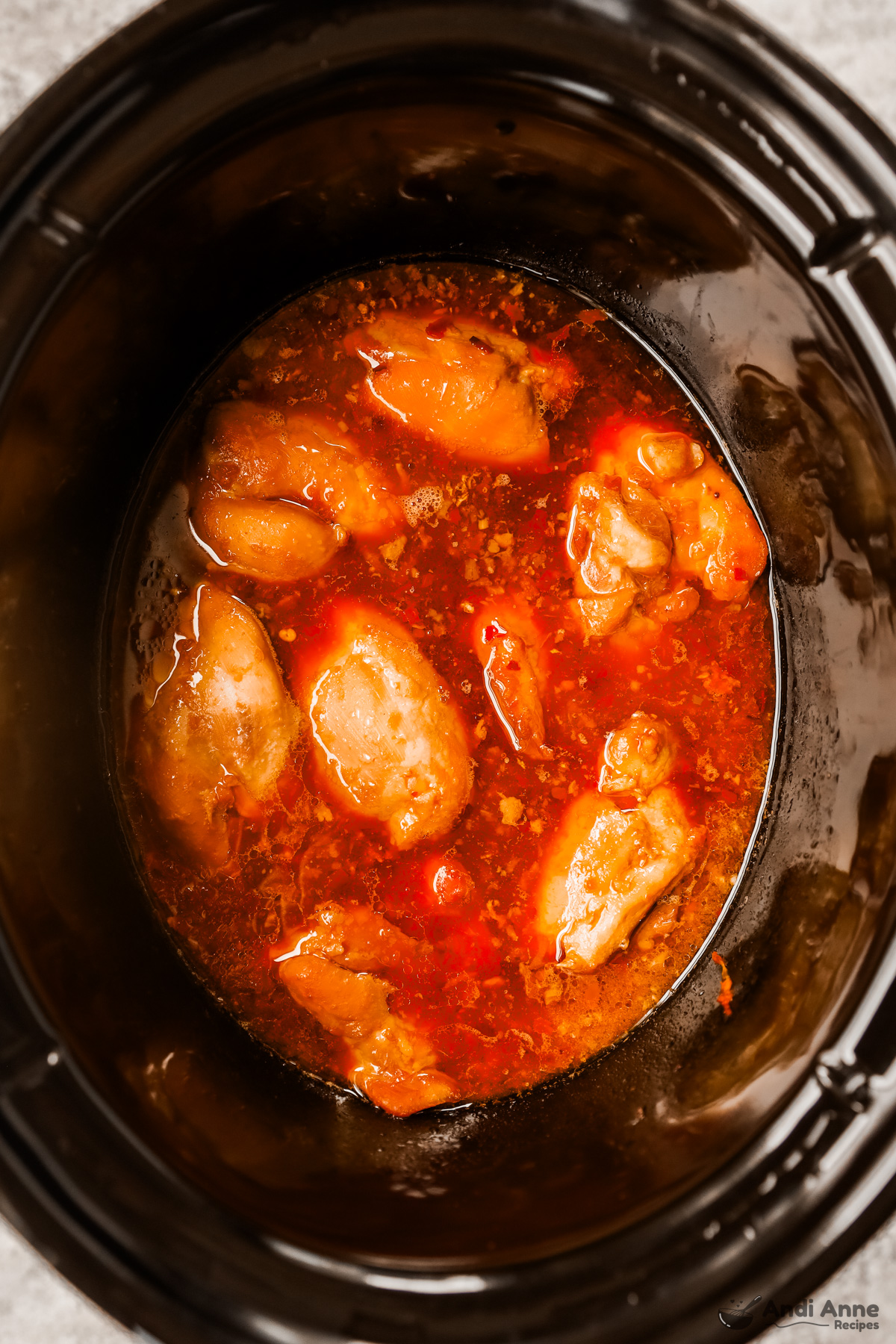 Looking into a crockpot with cooked chicken thighs in a red sauce.